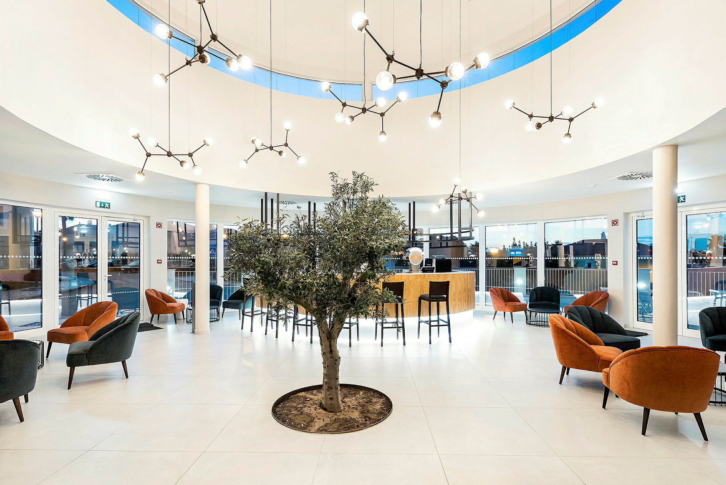 Modern reception med sittgrupper, ett olivträd och eleganta ljusarmaturer. (AI-genererad text)