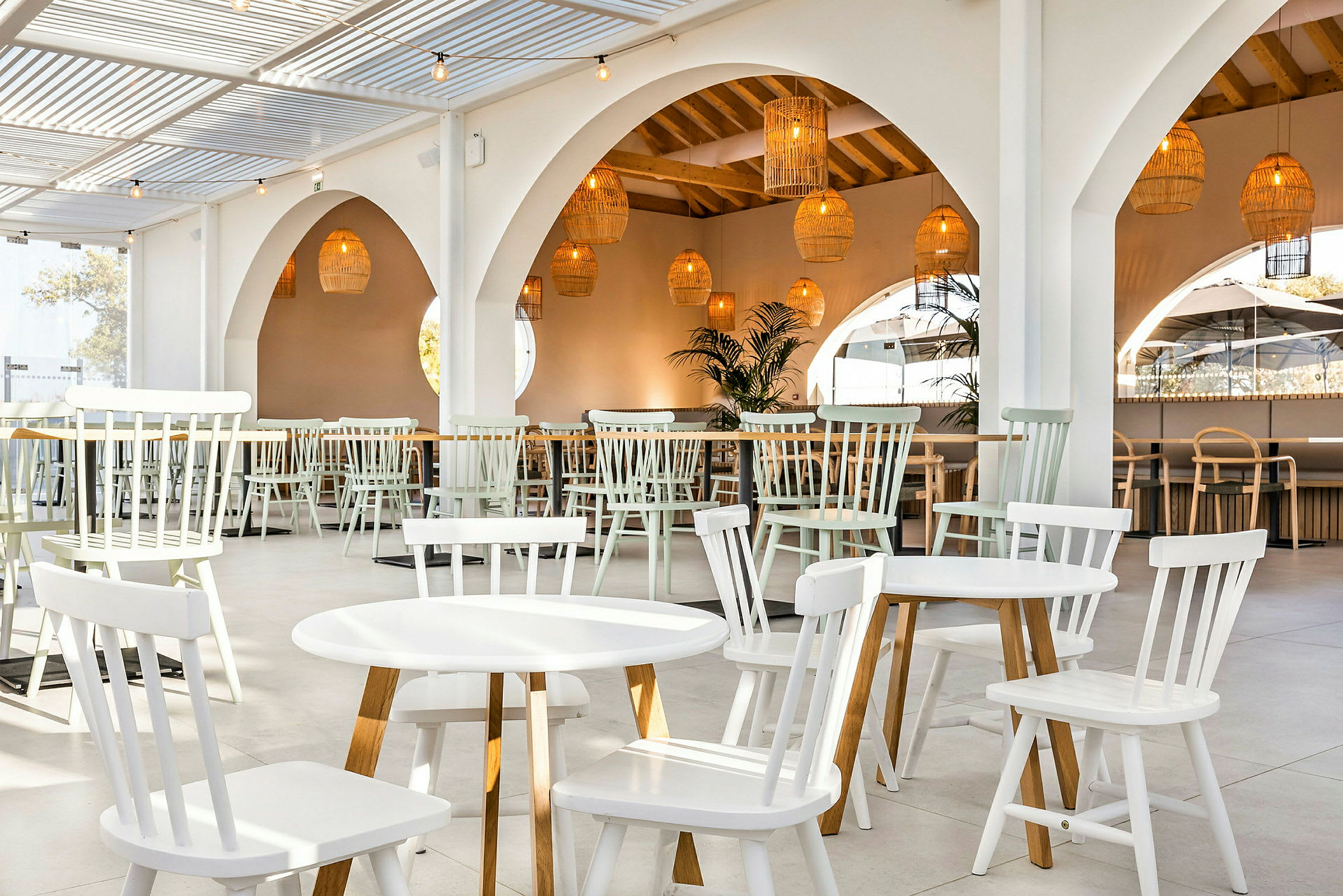 En ljus restaurang med vita träbord och stolar samt hängande korglampor. (AI-genererad text)