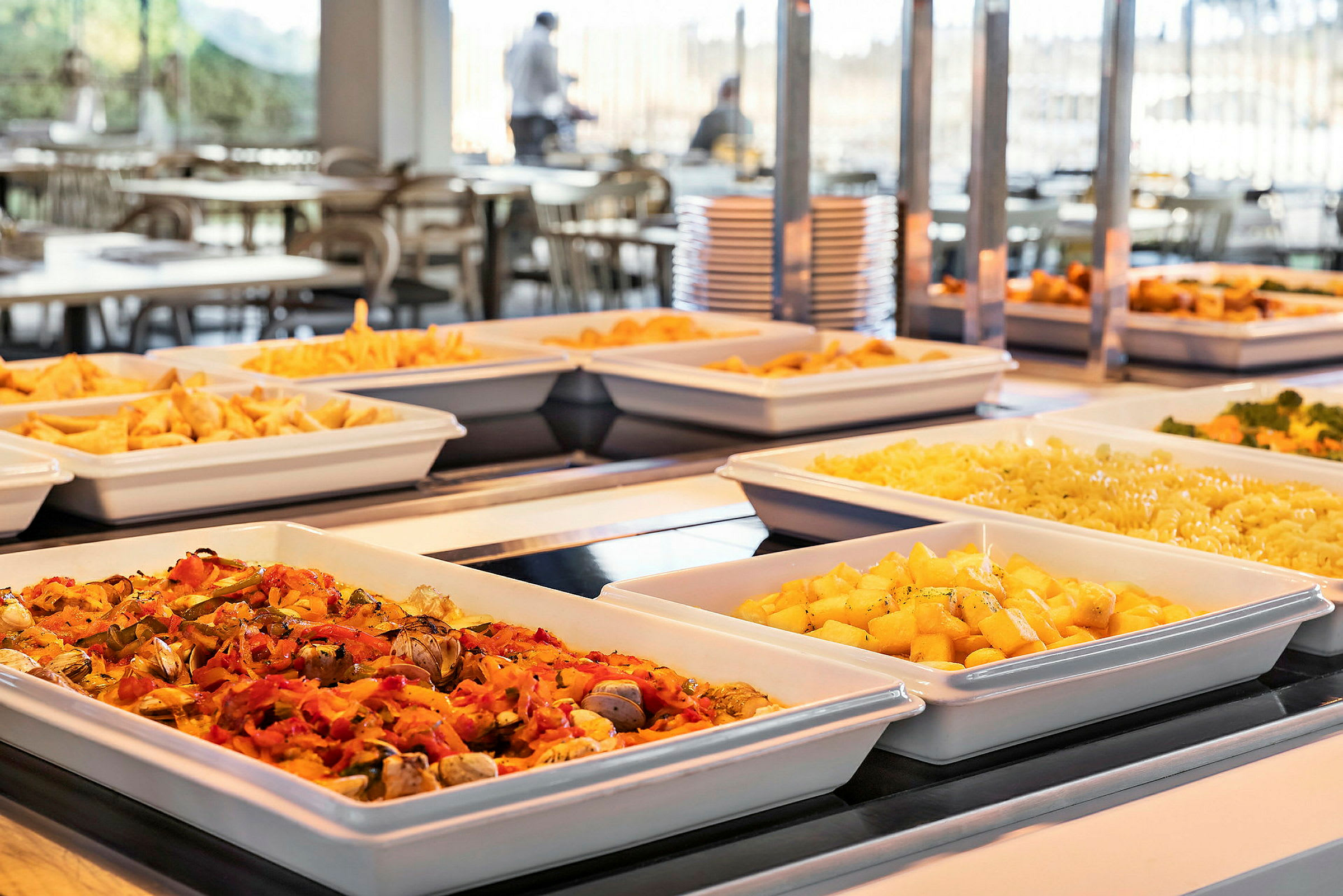Bild av en buffé med olika maträtter, inklusive potatis, pasta och grönsaker, upplagda i vita serveringsskålar. (AI-genererad text)