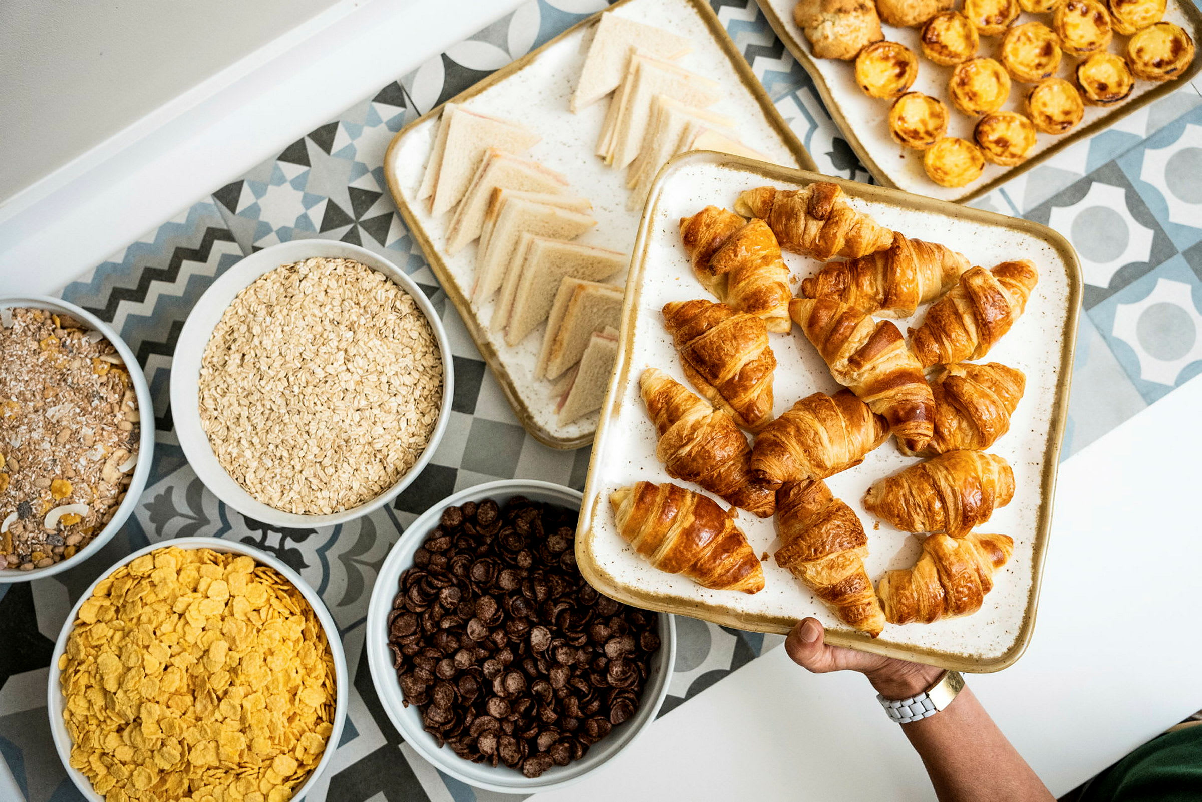 En bricka med croissanter samt olika skålar med spannmålsprodukter och andra bakverk. (AI-genererad text)