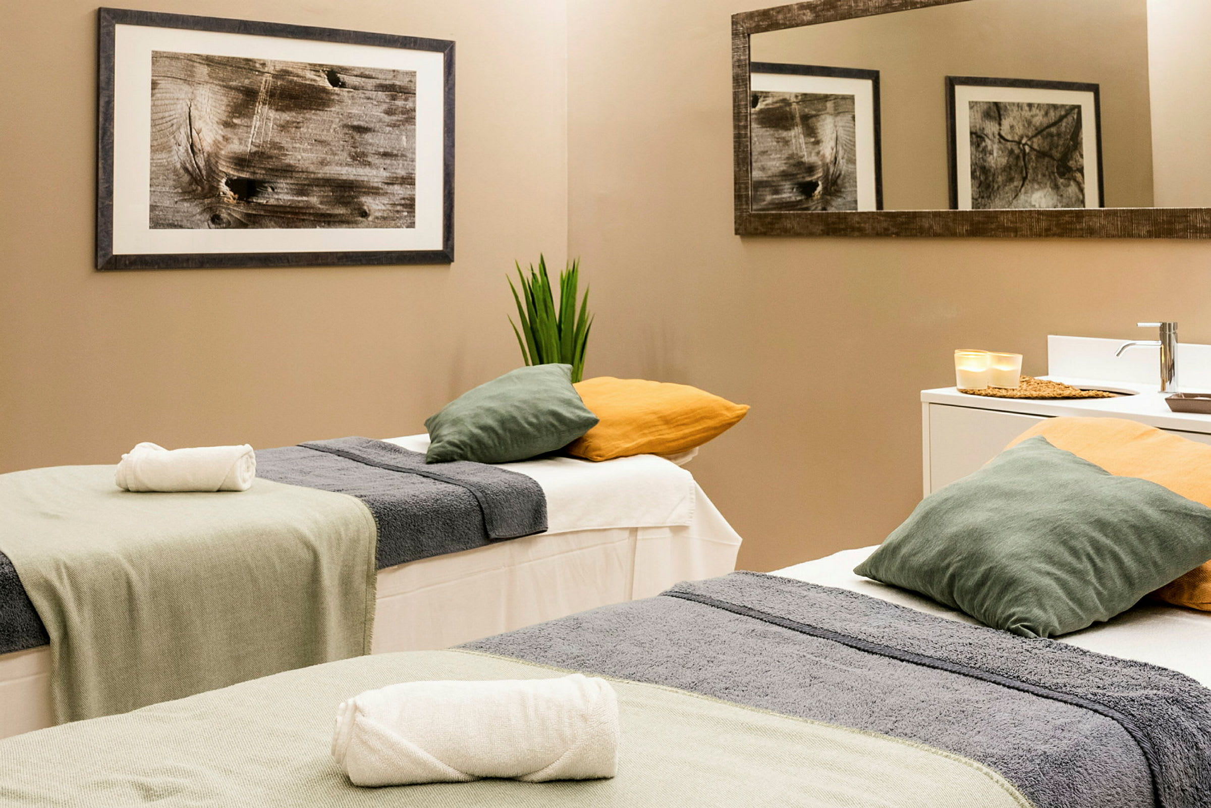 Två massagebänkar med handdukar och kuddar i ett ljust rum. (AI-genererad text)