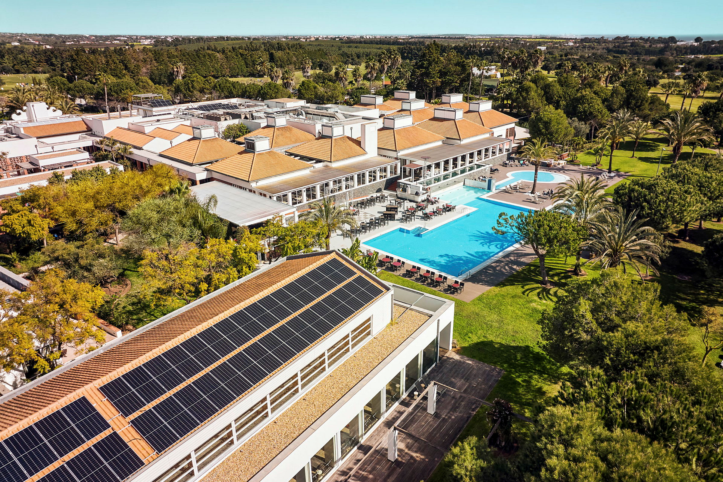 Luftvy av en semesteranläggning med pool, trädgårdar och byggnader med solpaneler på taket. (AI-genererad text)