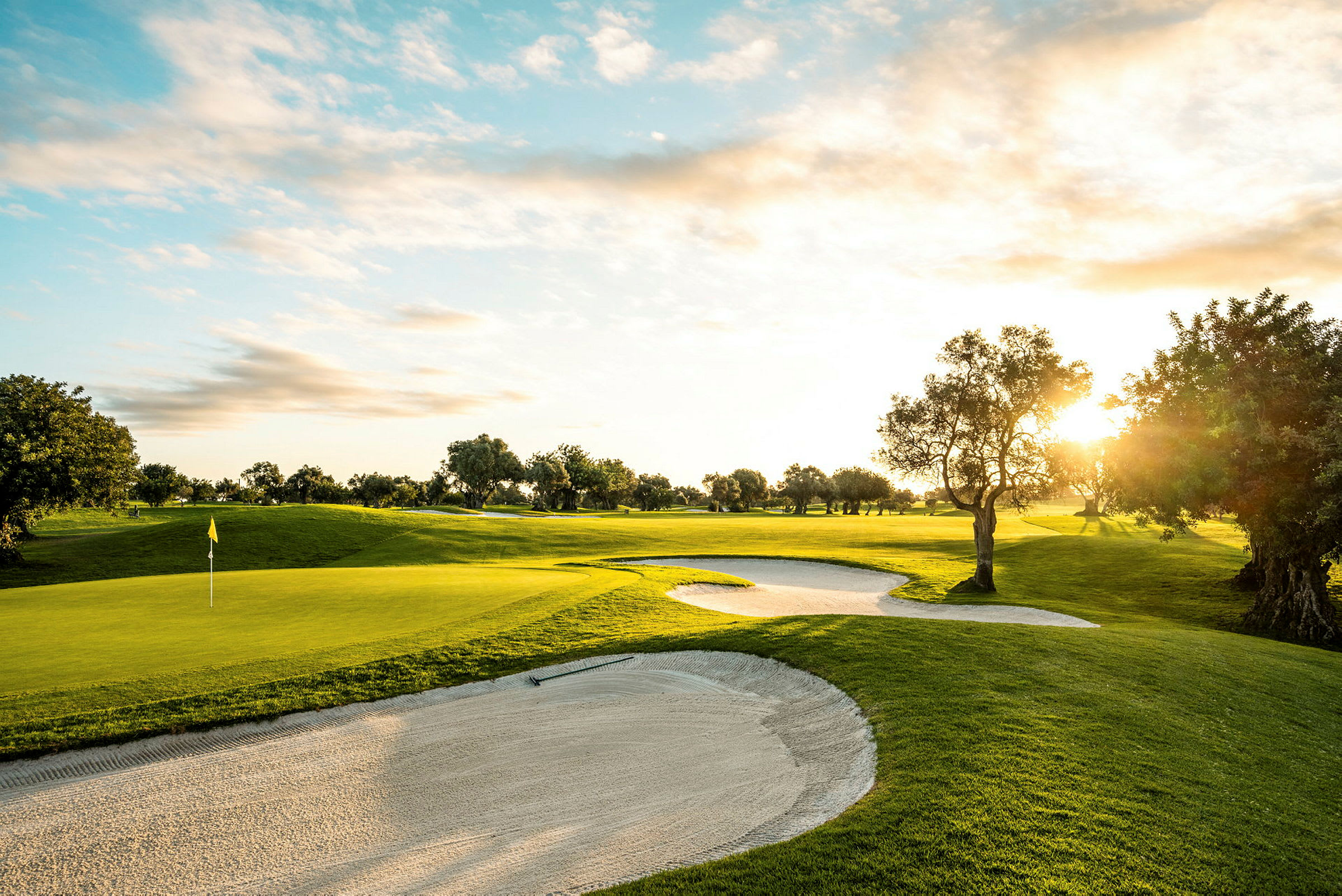 En golfbana med sandbunkrar, solnedgång och träd. (AI-genererad text)