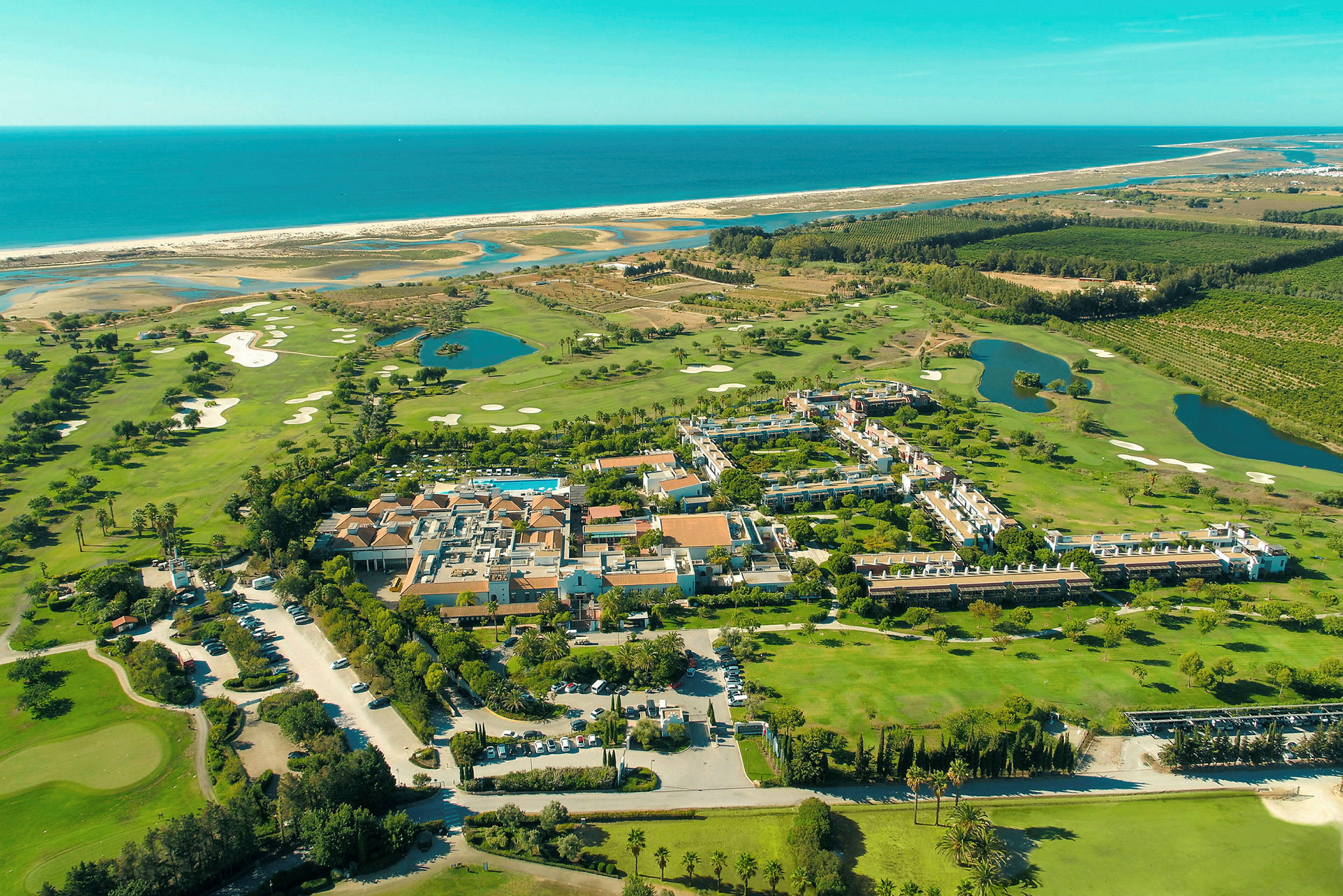 Flygfoto över en semesteranläggning omgiven av grönska, golfbanor och närhet till havet. (AI-genererad text)