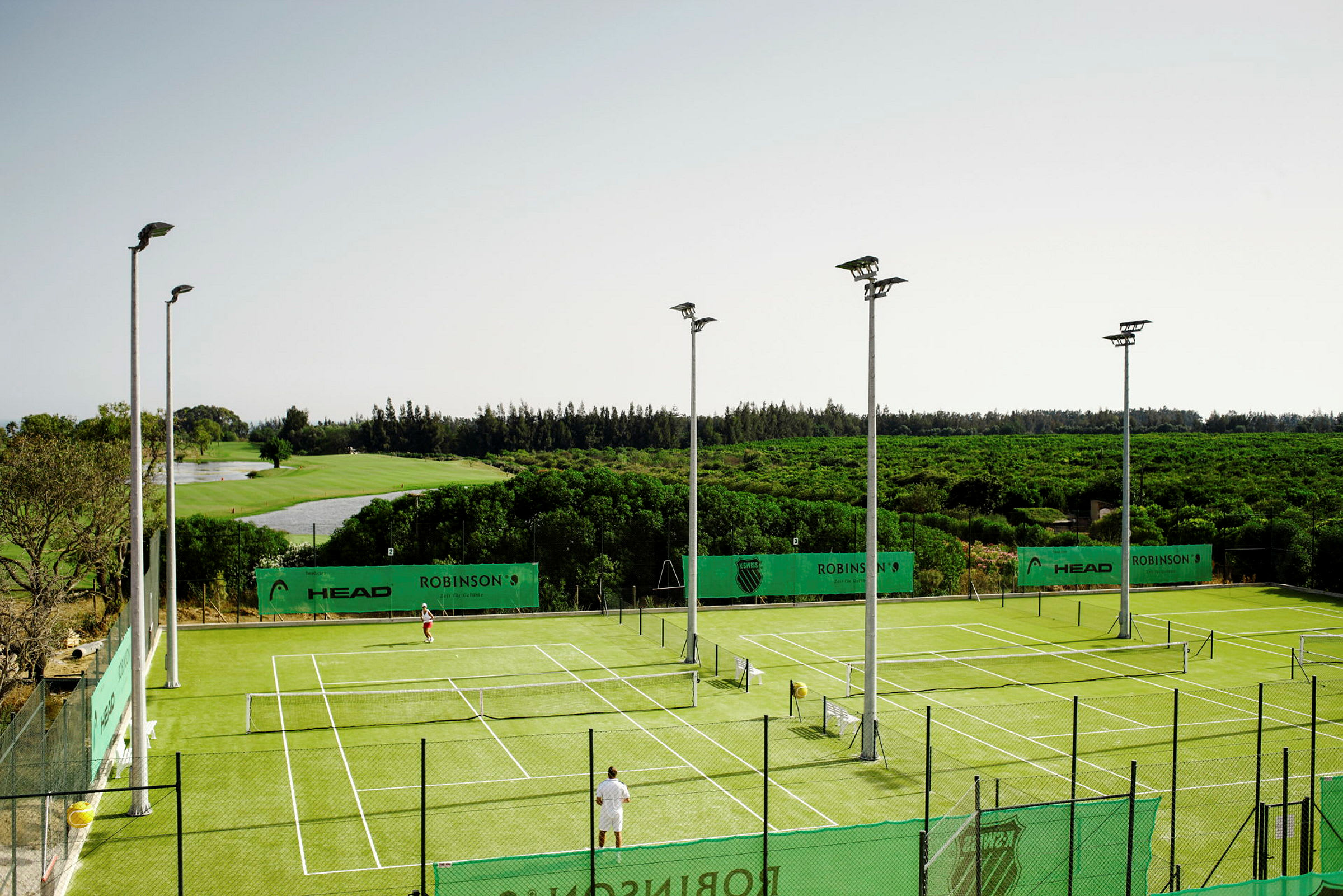 Tennisbanor med grönt underlag omgivna av grönska. (AI-genererad text)