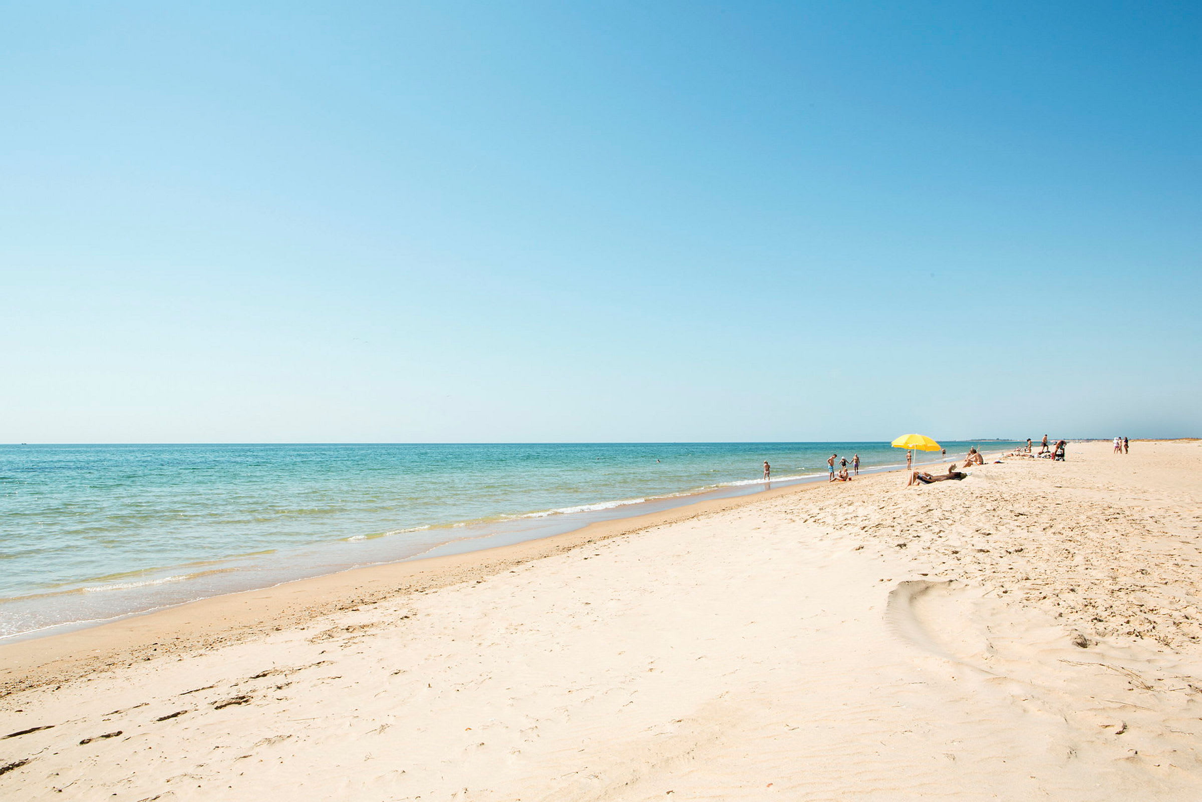 En sandstrand med människor i solen och hav i bakgrunden. (AI-genererad text)