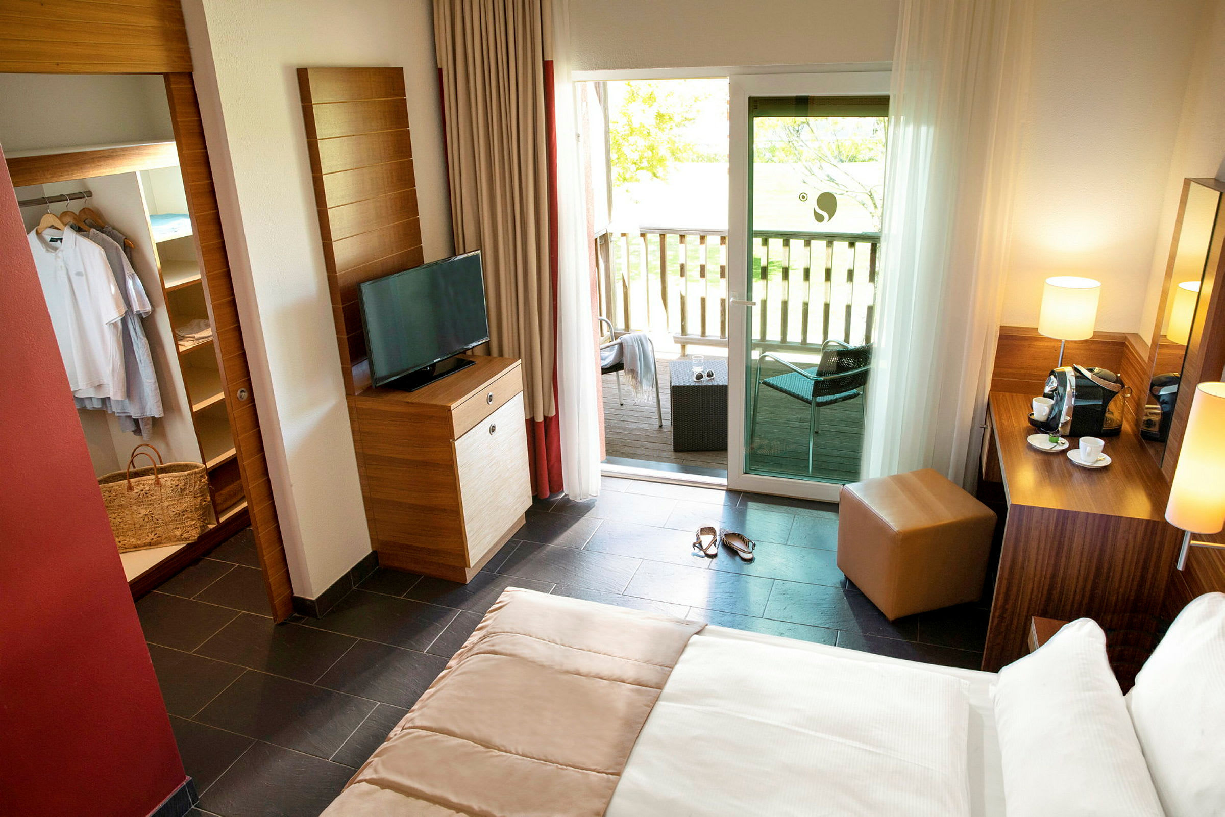 En ljus hotellrum med säng, TV, en garderob och en balkong med sittgruppen utanför. (AI-genererad text)