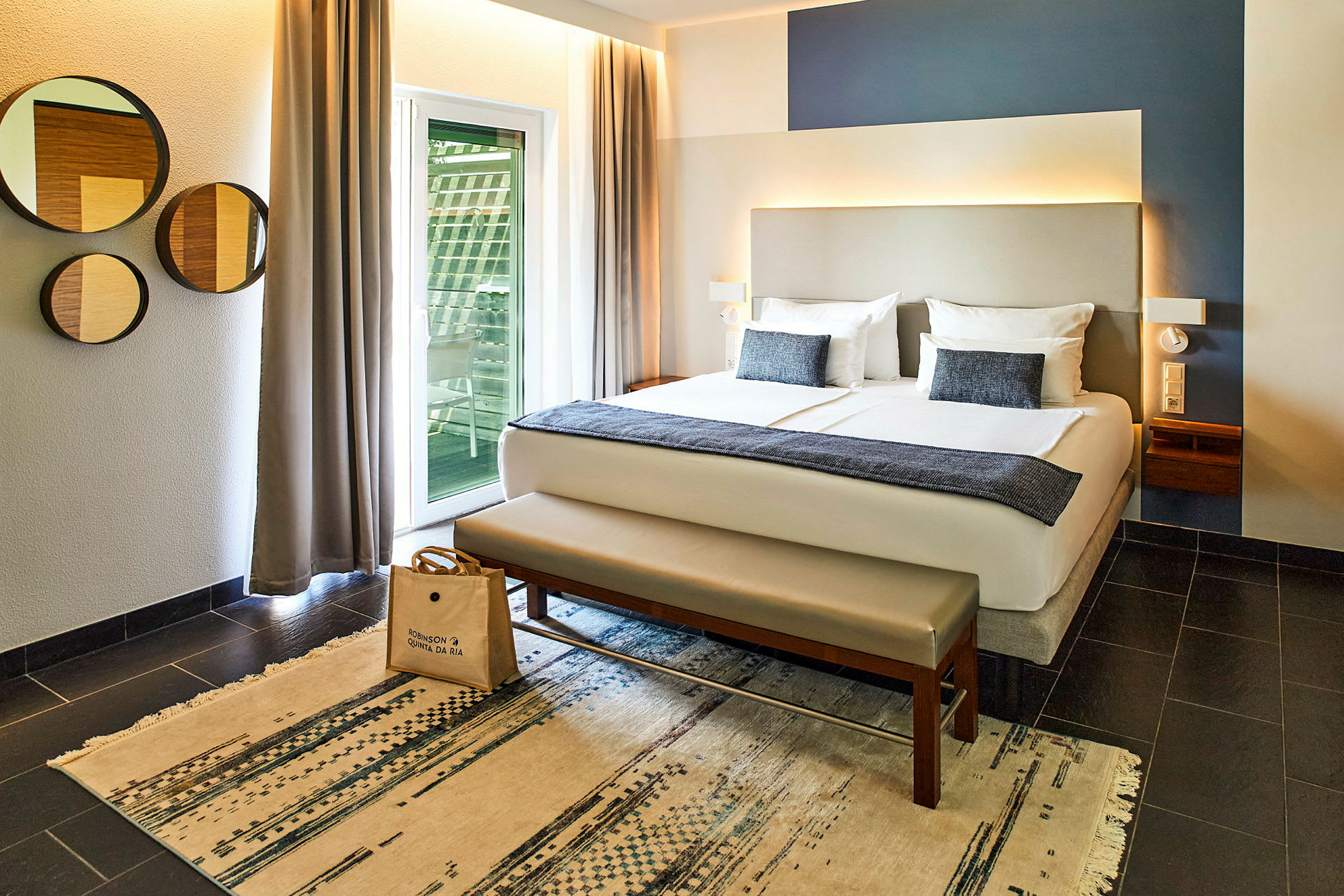 Ett modernt hotellrum med en stor säng, en bänk vid fotändan och en dörr som leder till en balkong. (AI-genererad text)