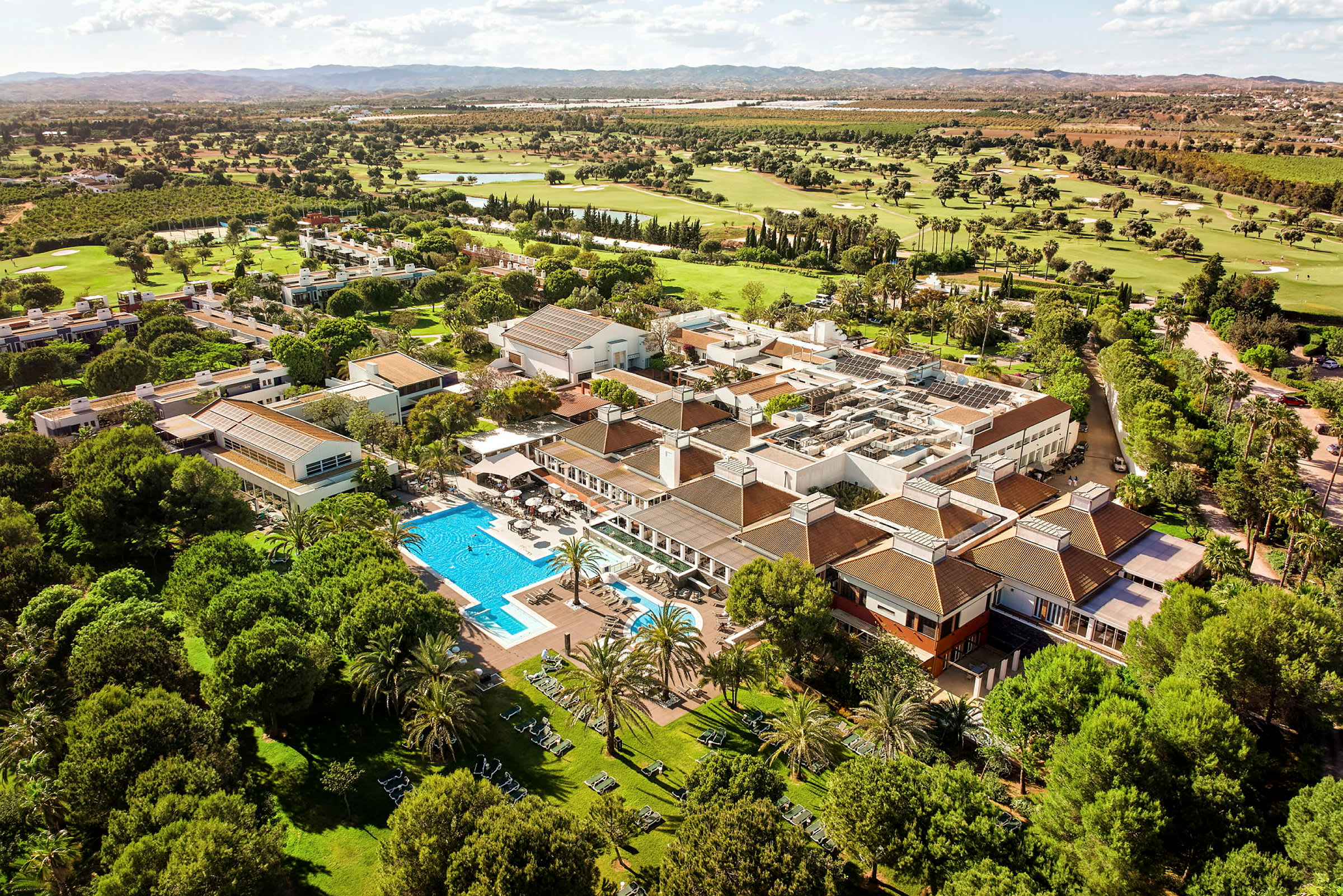 Flygvy över ett semesterkomplex med pool, omgivande grönområden och golfbanor. (AI-genererad text)
