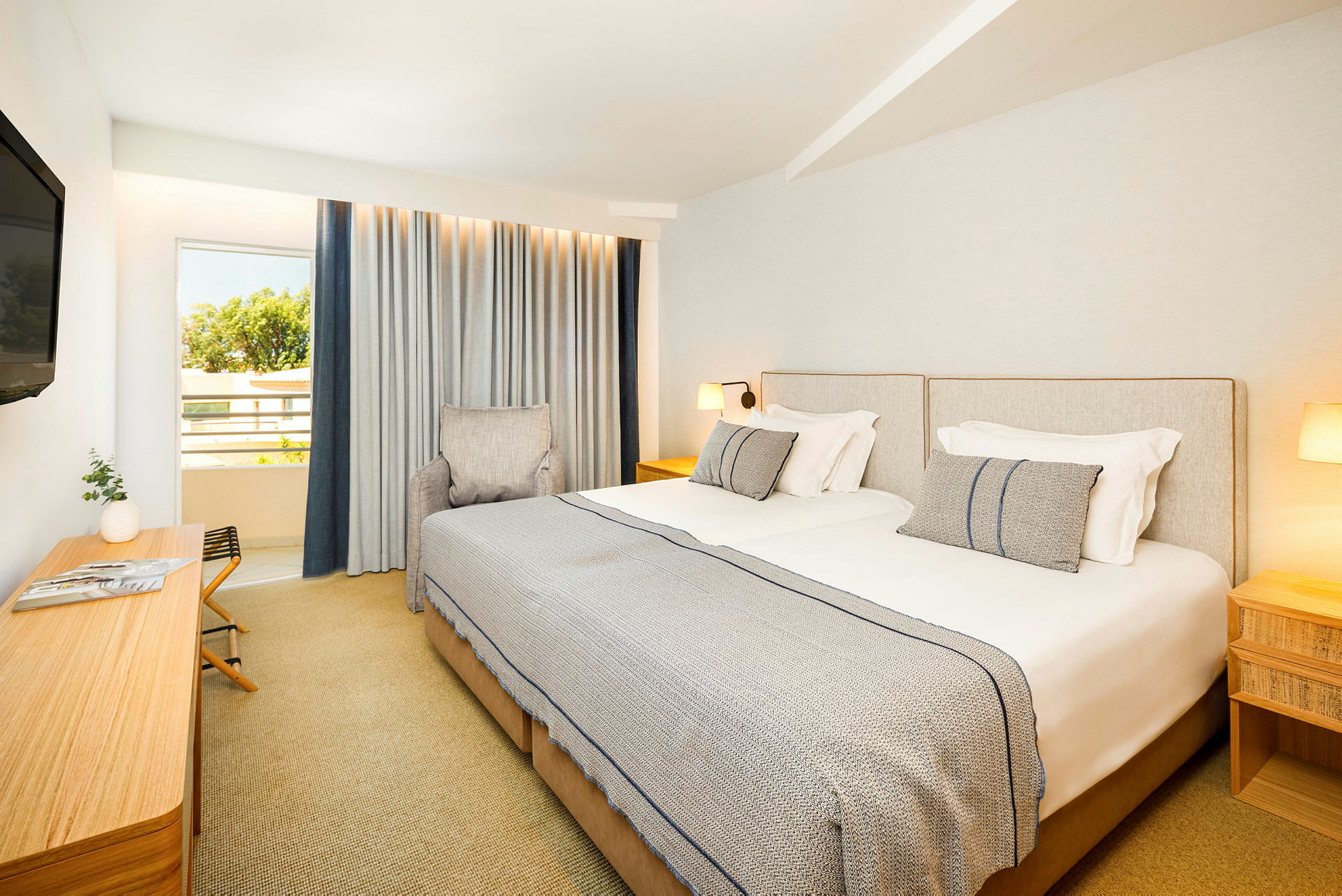 Hotellrum med två enkelsängar, en stol, en skrivbord och en TV, samt ett fönster med gardiner. (AI-genererad text)