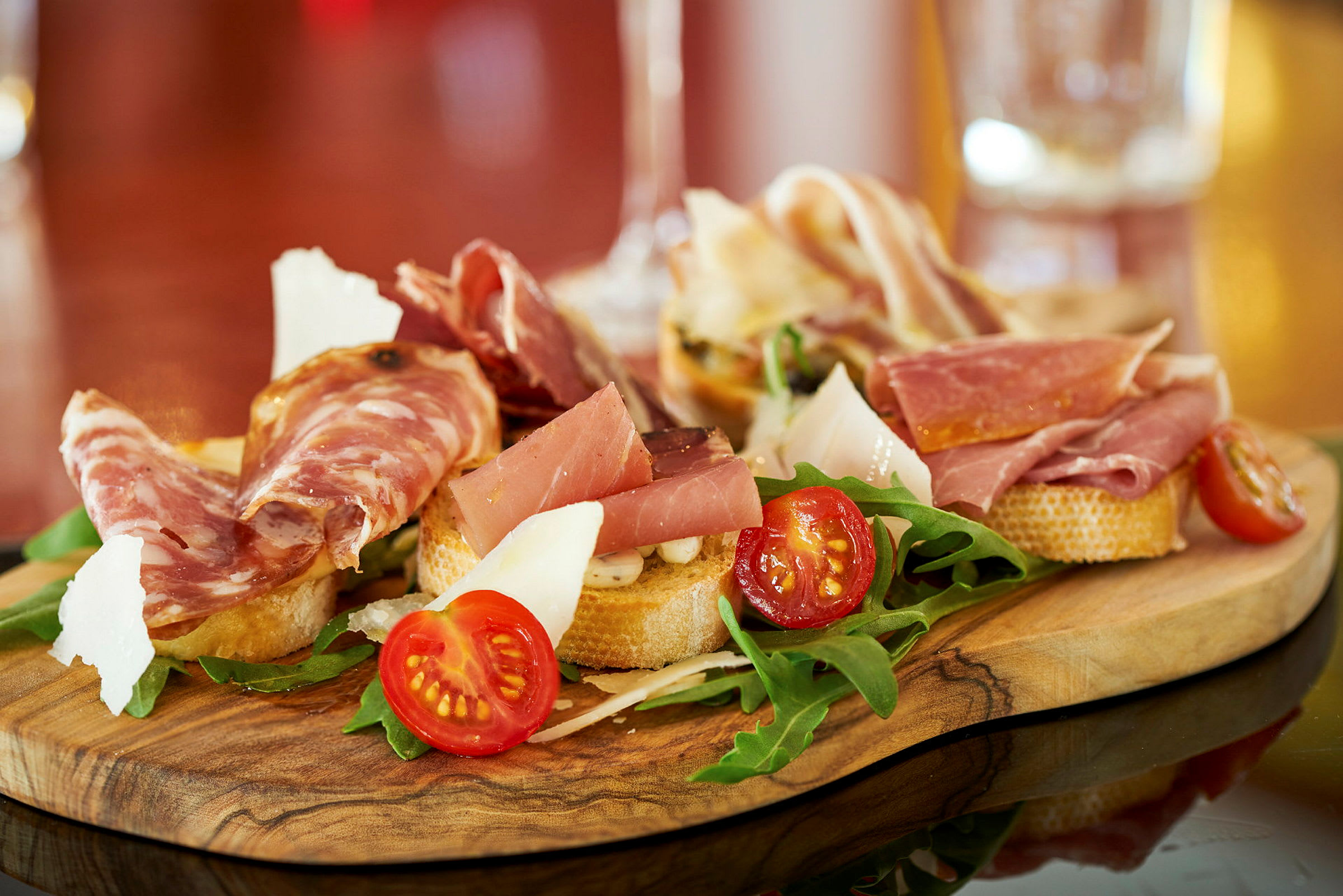 En träbricka med antipasti som inkluderar skivor av kallskuret, körsbärstomater, ruccola och ost. (AI-genererad text)