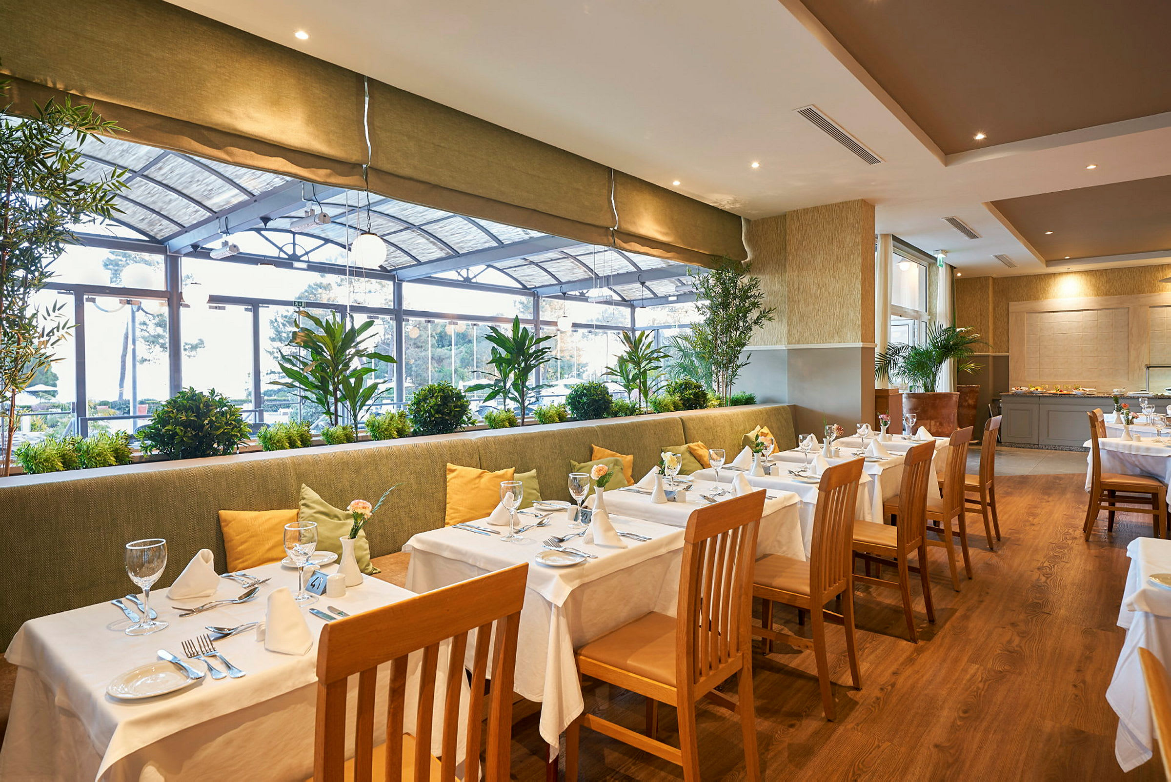 Restaurang med dukade bord, stolar och grönska vid fönstren. (AI-genererad text)