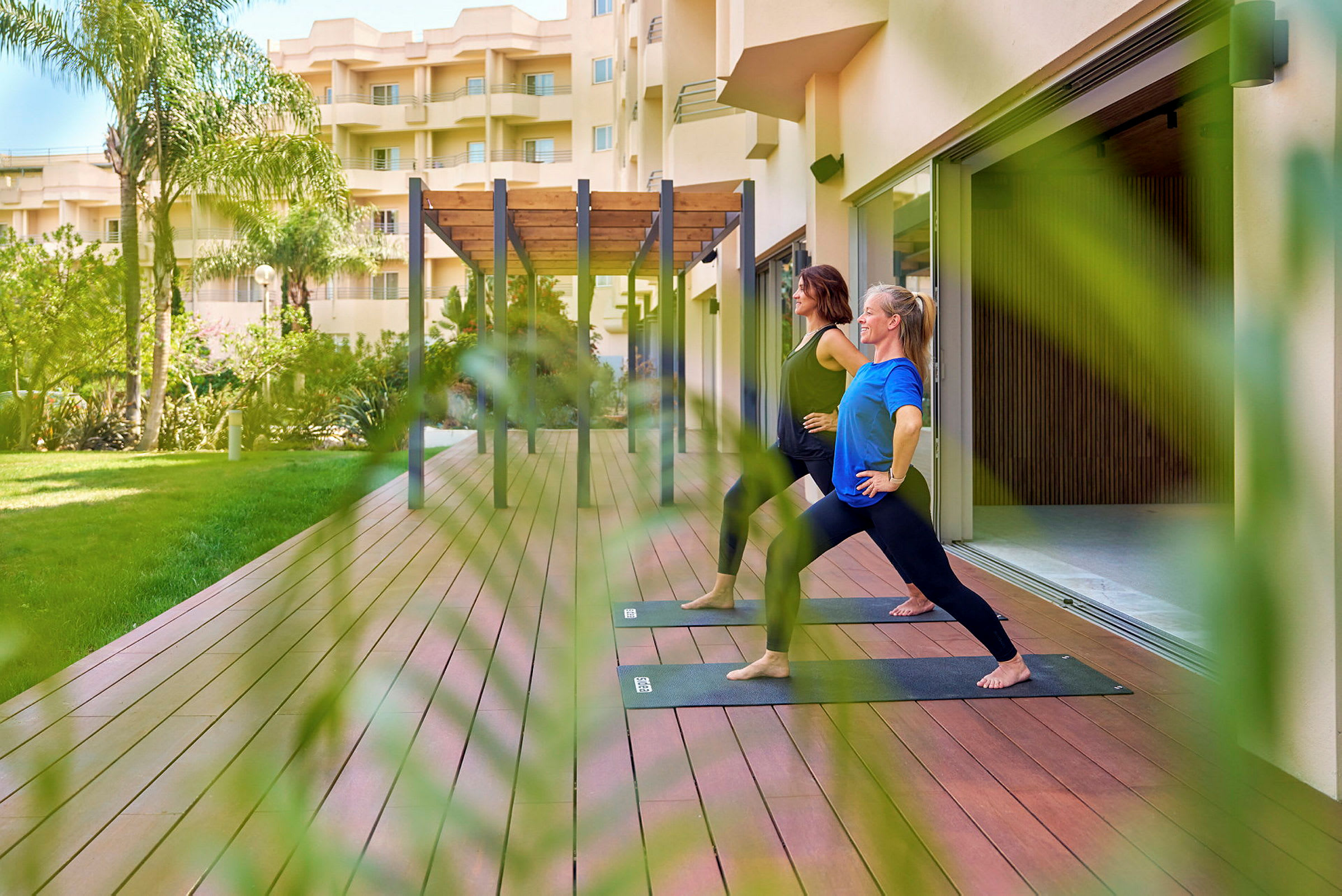 Personer utövar yoga på en träplattform utomhus nära en byggnad. (AI-genererad text)