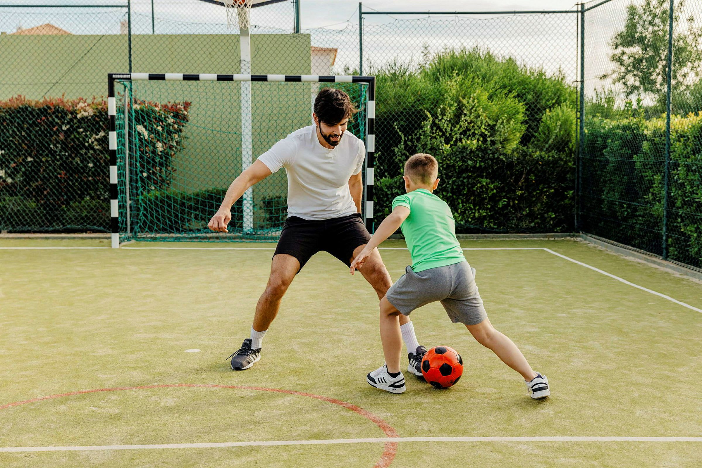Två personer spelar fotboll på en liten konstgräsplan. (AI-genererad text)
