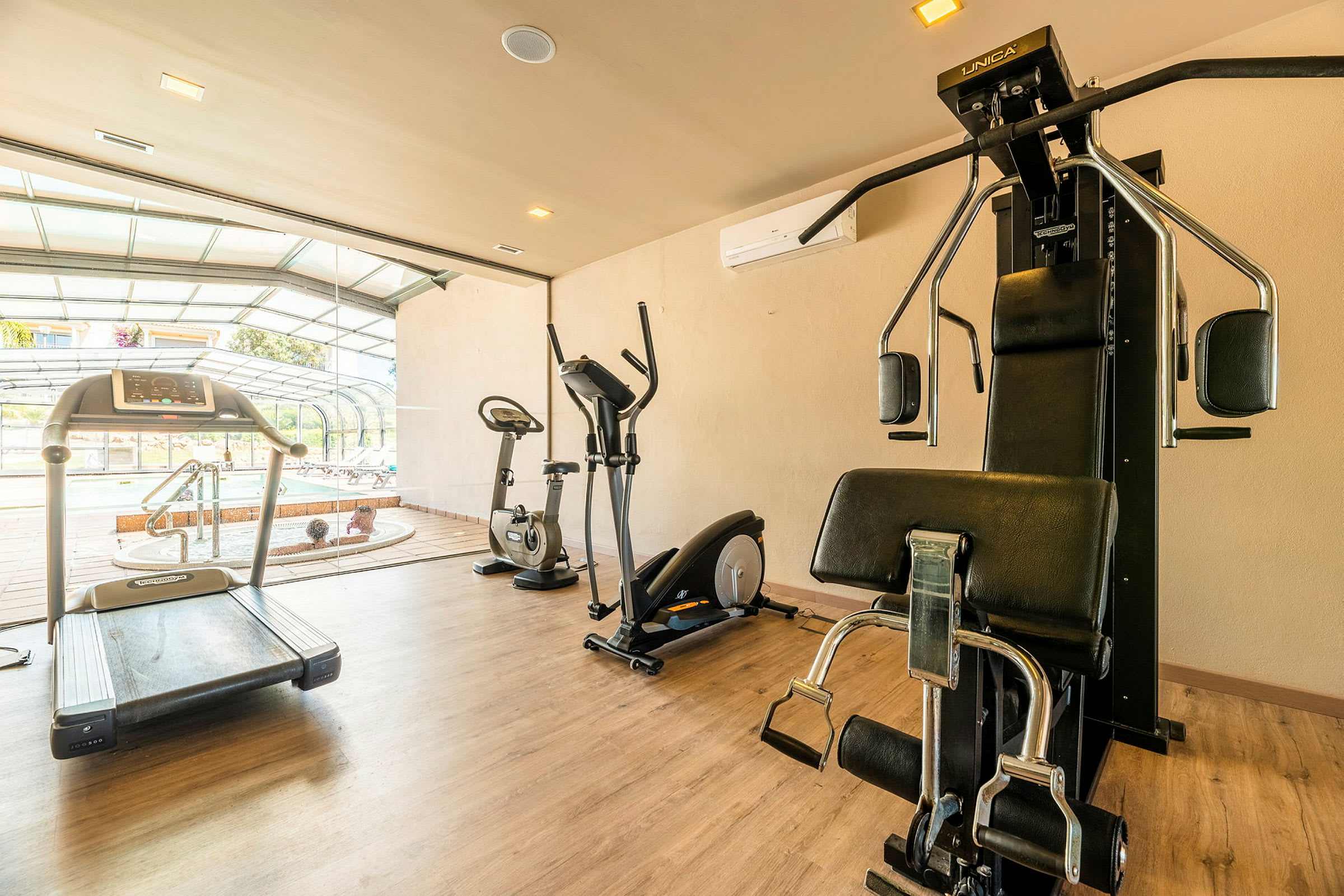 Bild av ett gym med löpband, träningscyklar och styrketräningsutrustning. I bakgrunden syns en bubbelpool och en terrass. (AI-genererad text)