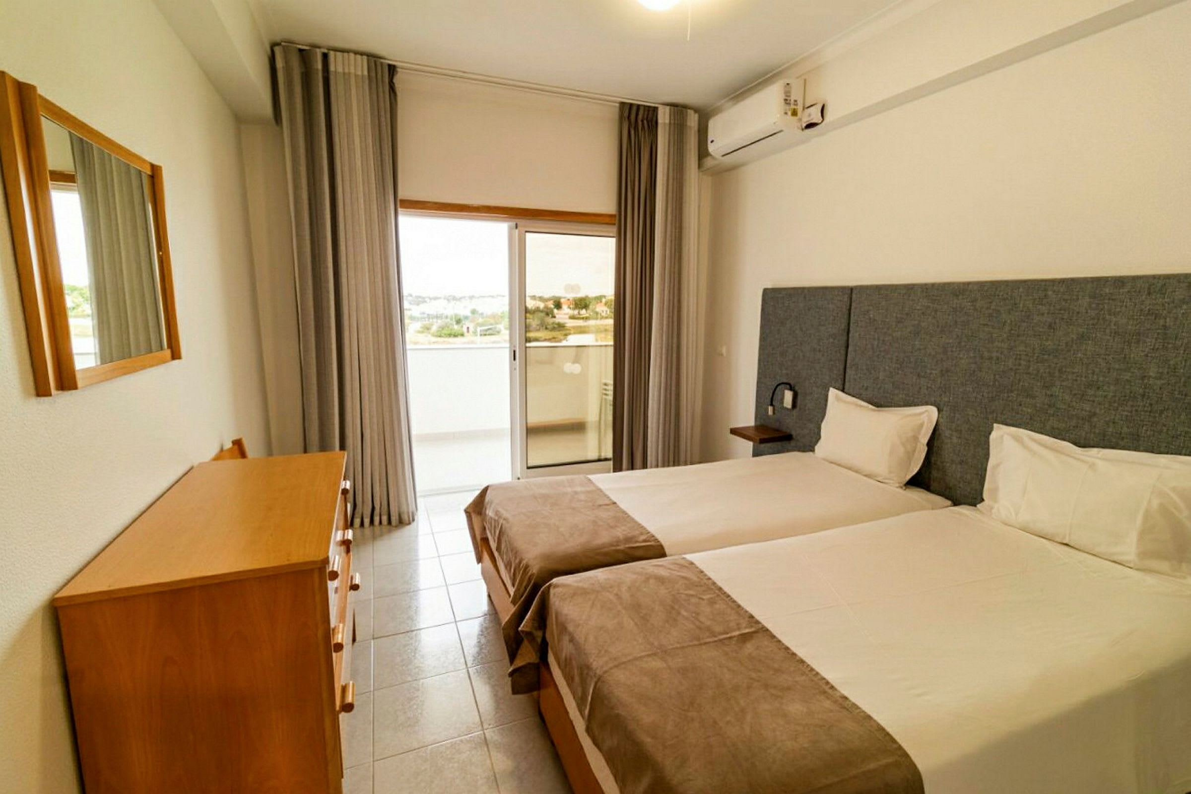 En hotellrum med två enkelsängar, en byrå med spegel samt en glasdörr som leder till balkongen. (AI-genererad text)