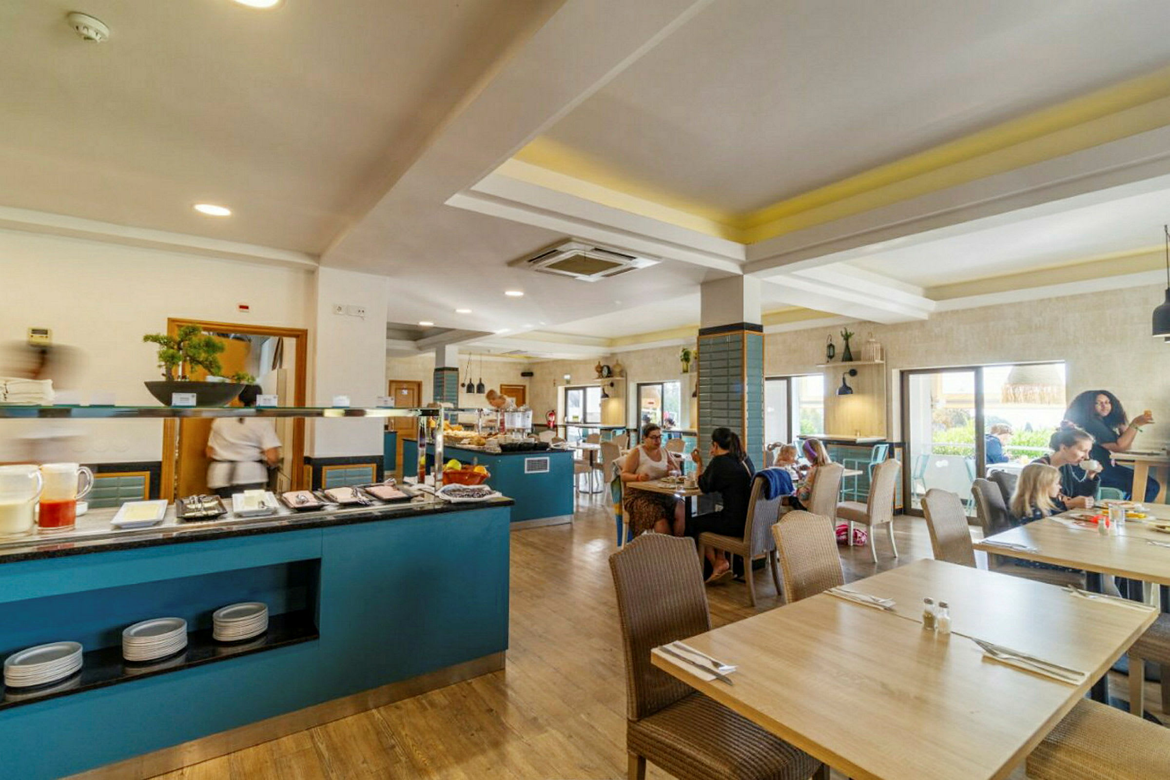 Restaurangmiljö med bord och människor, samt en buffédisk med mat och drycker. (AI-genererad text)