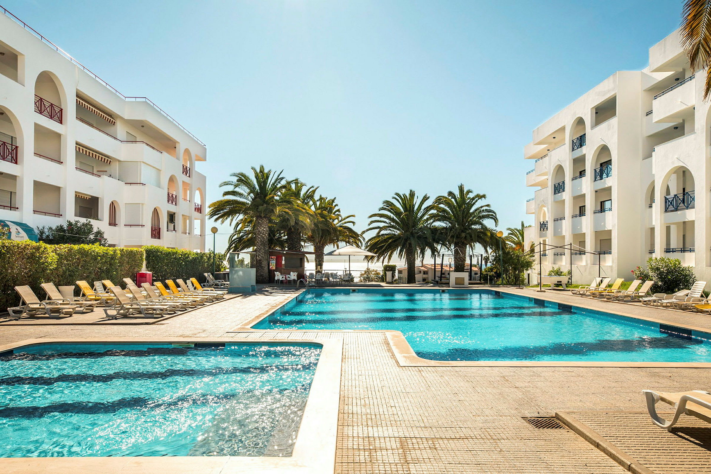 Utomhuspool omgiven av solstolar och palmer vid ett hotell. (AI-genererad text)