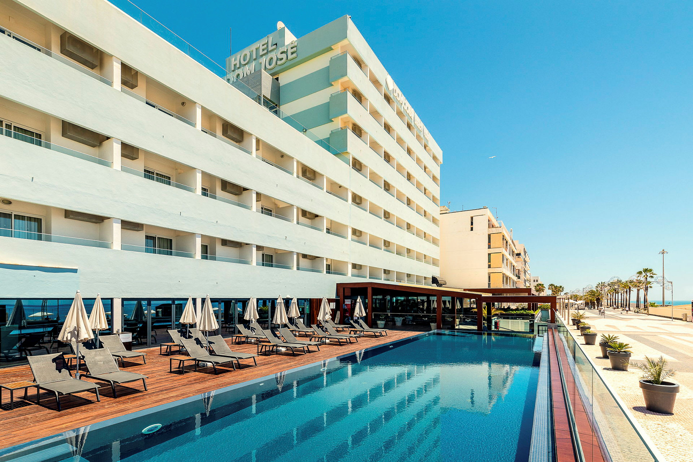 Hotellbyggnad med pool och solstolar. (AI-genererad text)