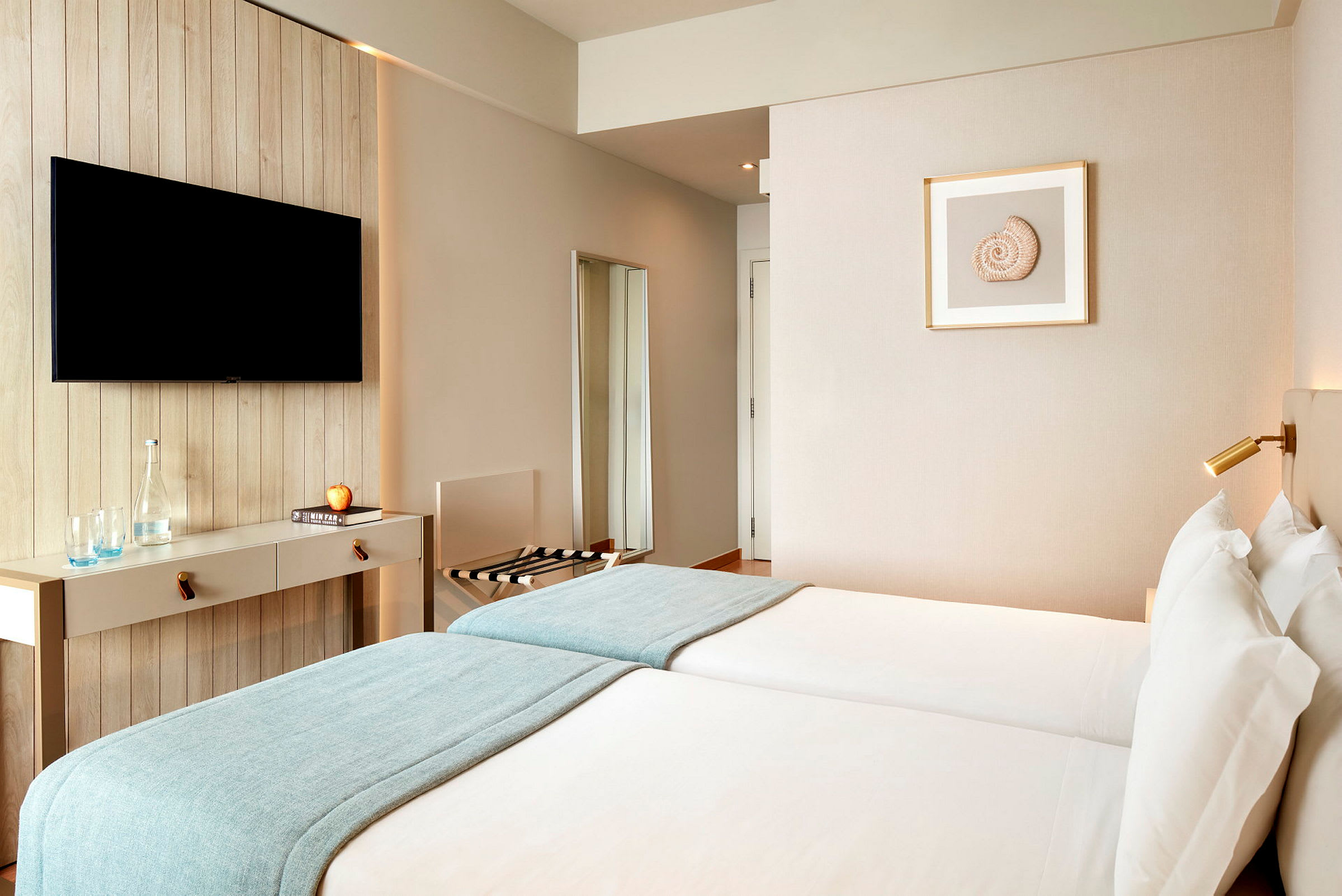 Ett hotellrum med två enkelsängar, en väggmonterad TV och minimalistisk inredning. (AI-genererad text)