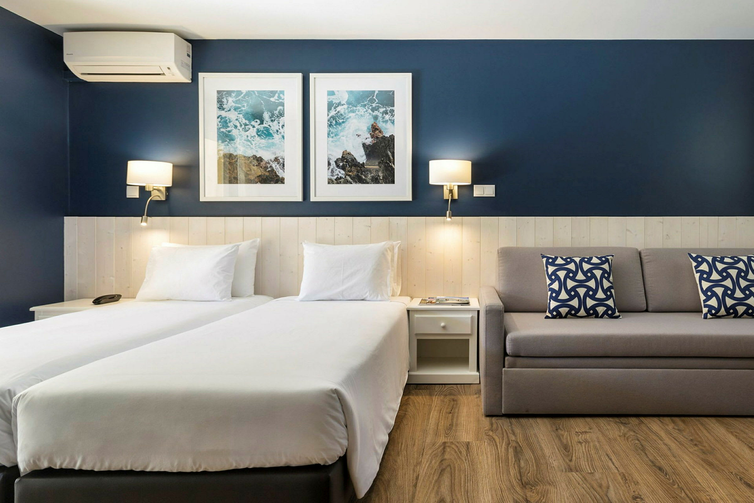 Hotellrum med två enkelsängar, en soffa och blå väggdekorationer. (AI-genererad text)