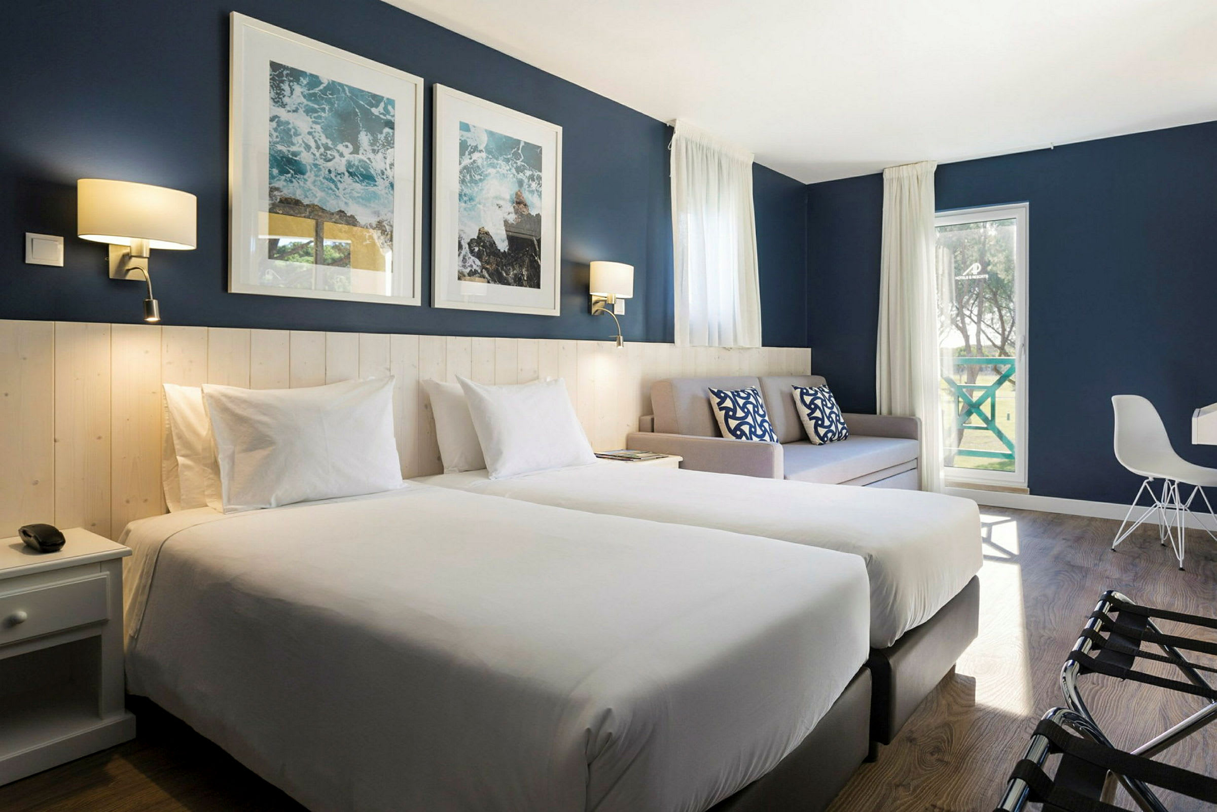 Ett hotellrum med två enkelsängar, en soffa, och blå dekorväggar. (AI-genererad text)