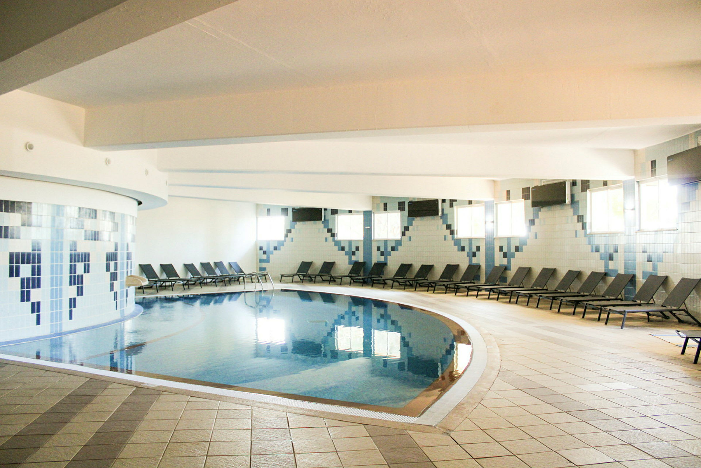 Inomhuspool med solstolar längs väggarna. (AI-genererad text)