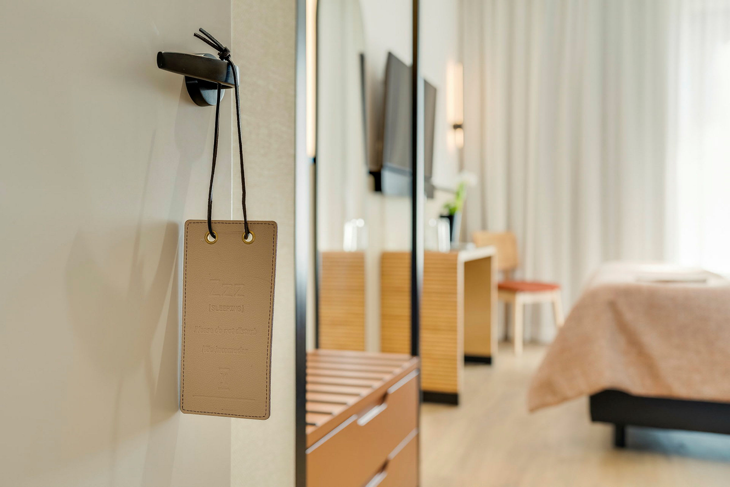 Skylt med texten 'Sover, stör ej' hängande på en dörr med en hotellrumsinredning i bakgrunden. (AI-genererad text)