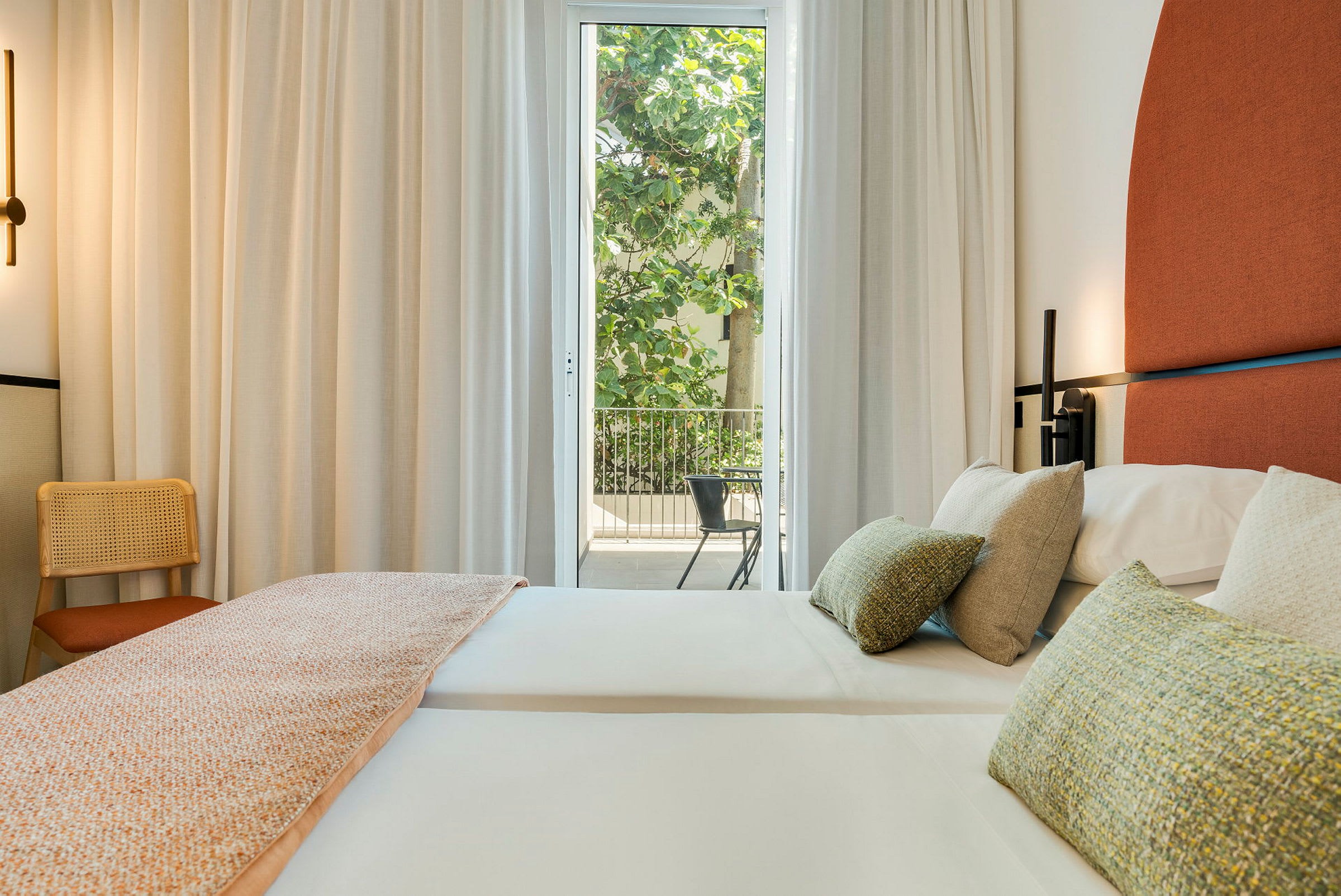 Hotellrum med två bäddade sängar och en möblerad balkong synlig genom glasdörrar. (AI-genererad text)