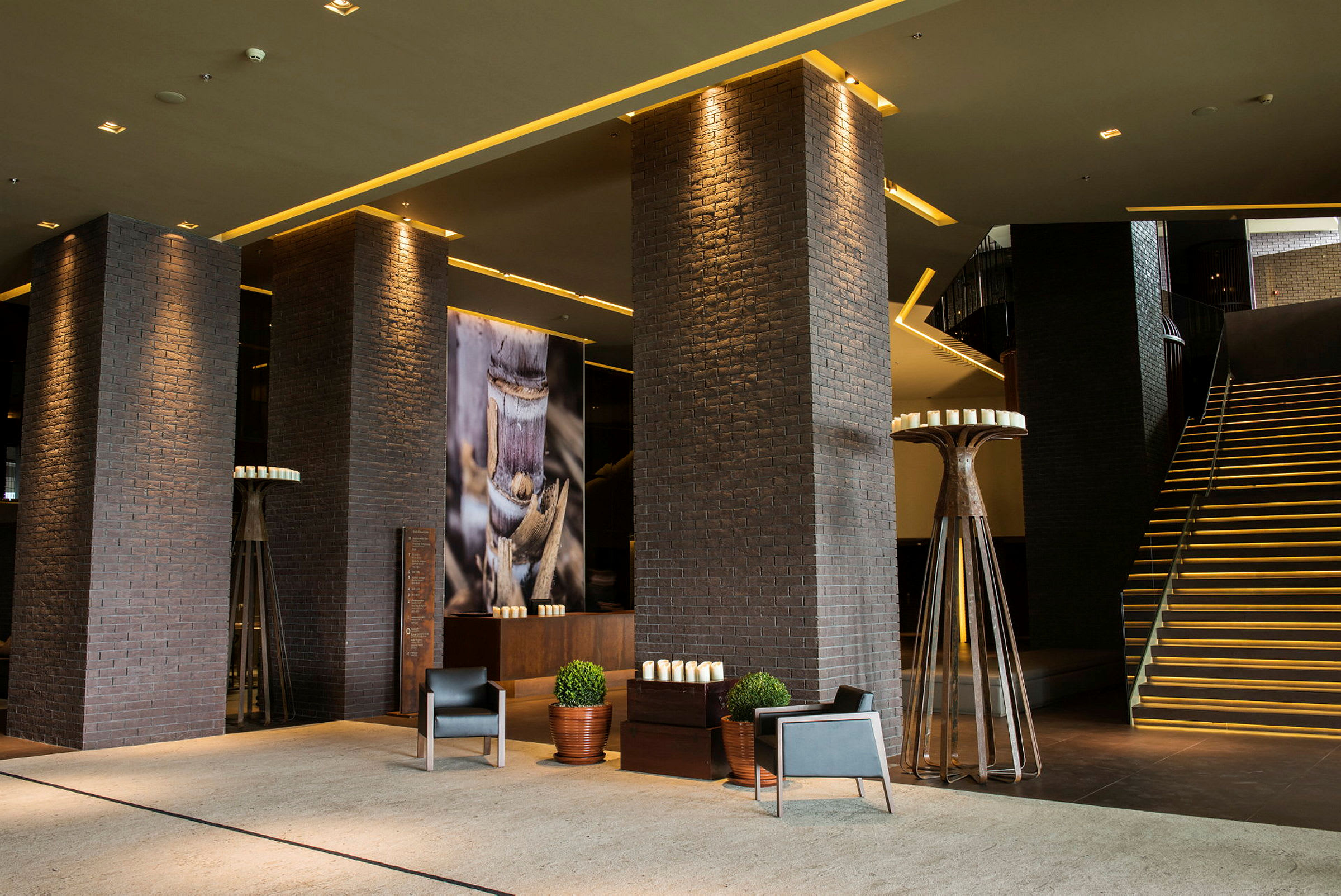 Ett modernt hotelllobby med mörka tegelpelare, dekorerade väggar och en upplyst trappa. (AI-genererad text)