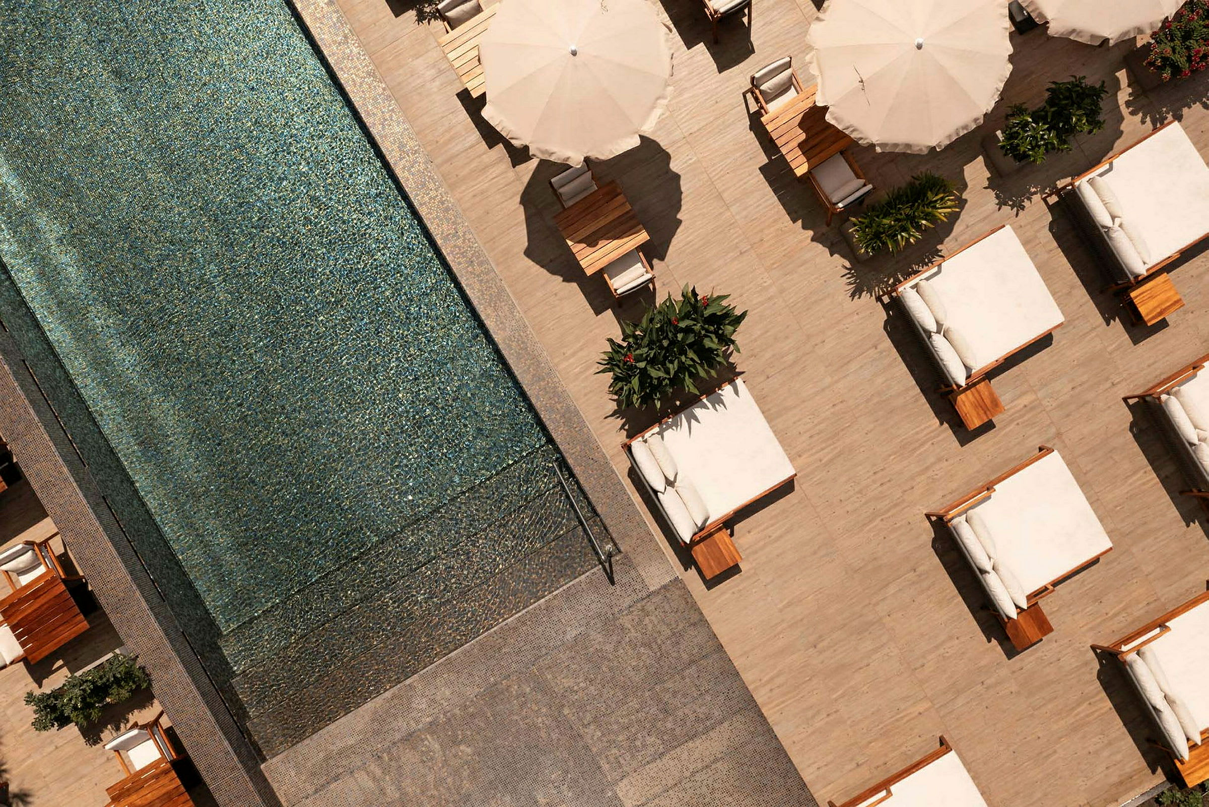 Vy ovanifrån av en pool bredvid en terrass med solsängar och parasoller. (AI-genererad text)