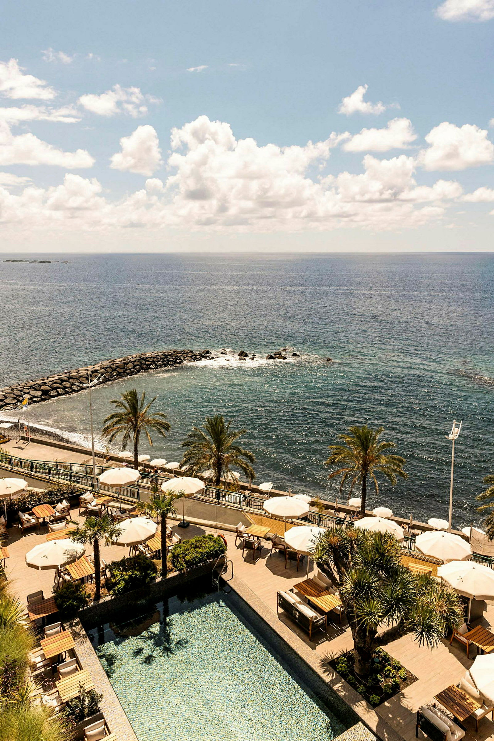 En resort med pool, parasoller, palmer och utsikt mot havet. (AI-genererad text)