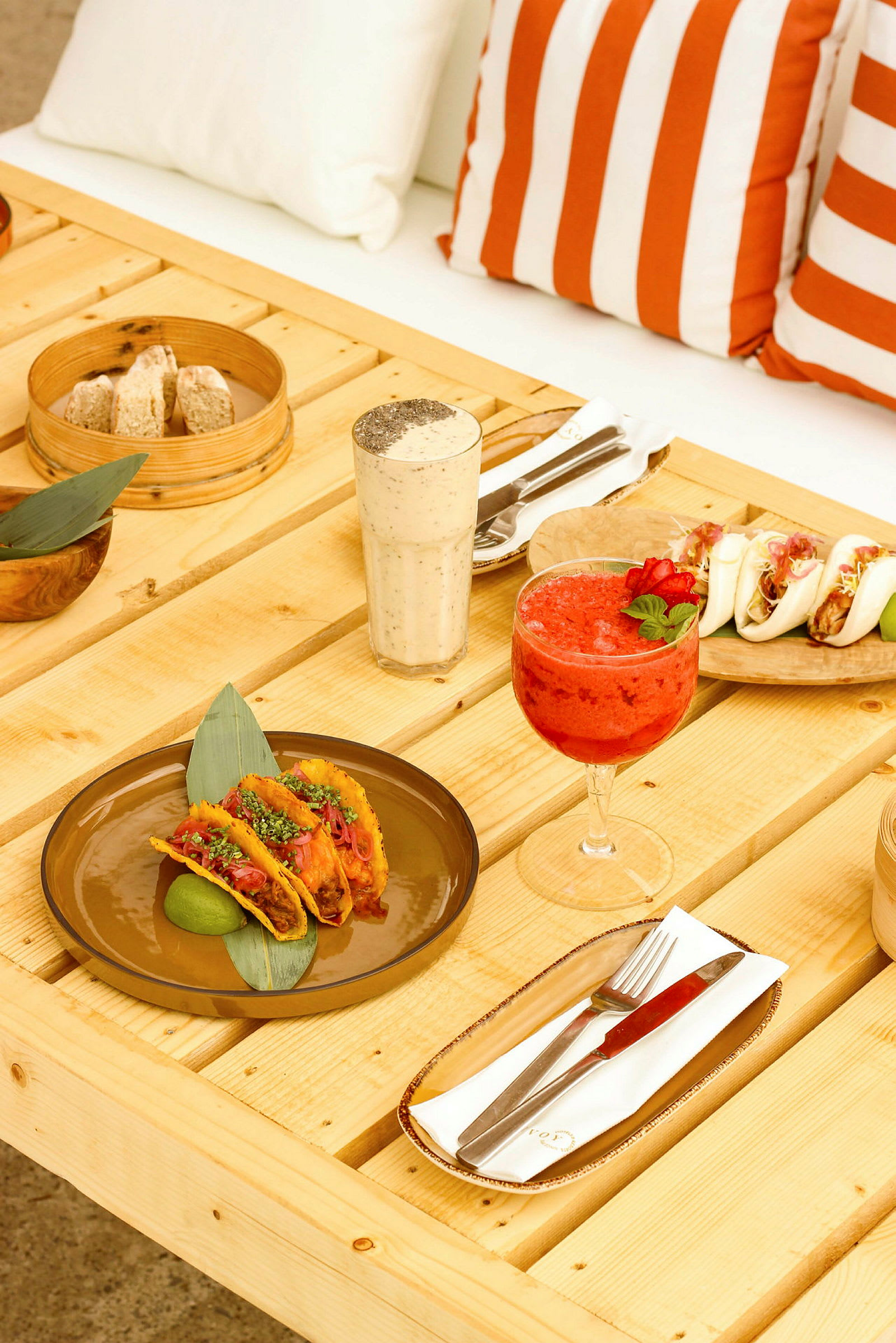 Ett bord med tacos, drycker och andra matvaror. Bakom finns orangevit randiga kuddar. (AI-genererad text)