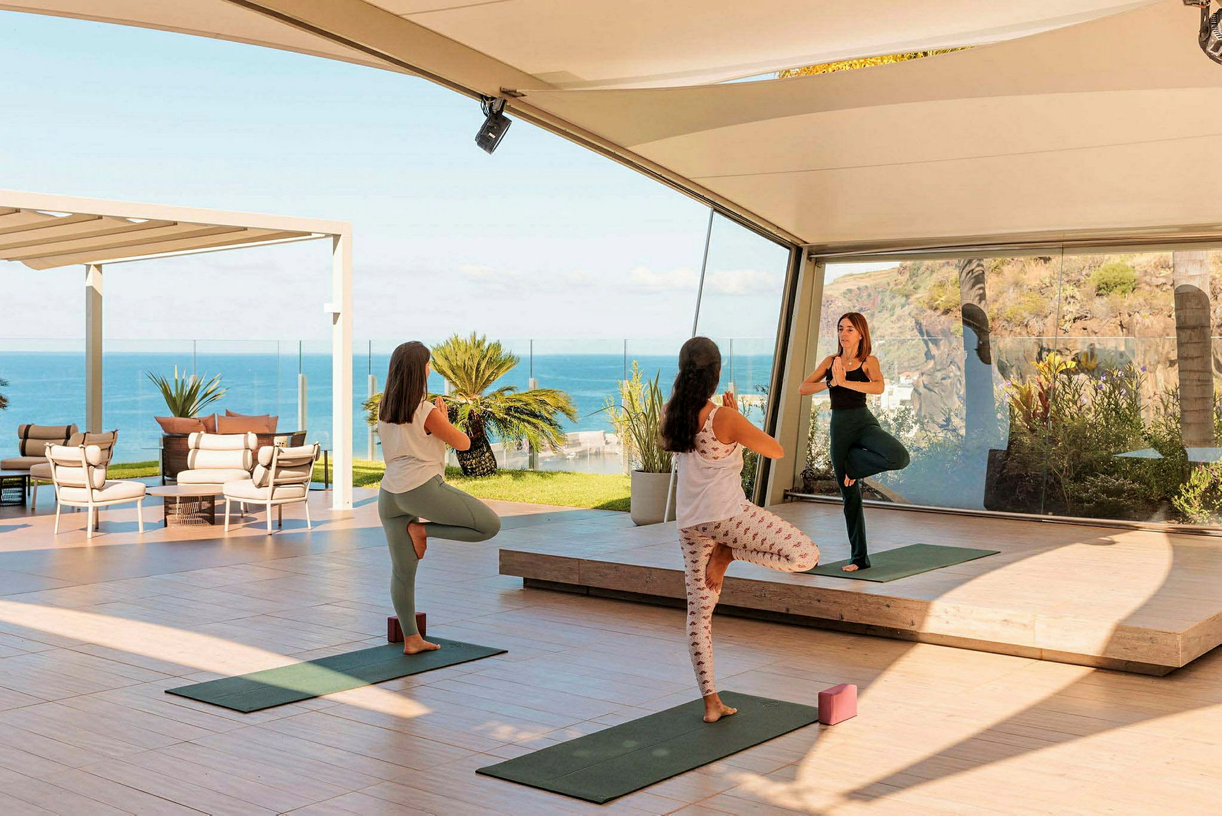 Tre personer utför yoga i en öppen och ljus miljö med havsutsikt. (AI-genererad text)