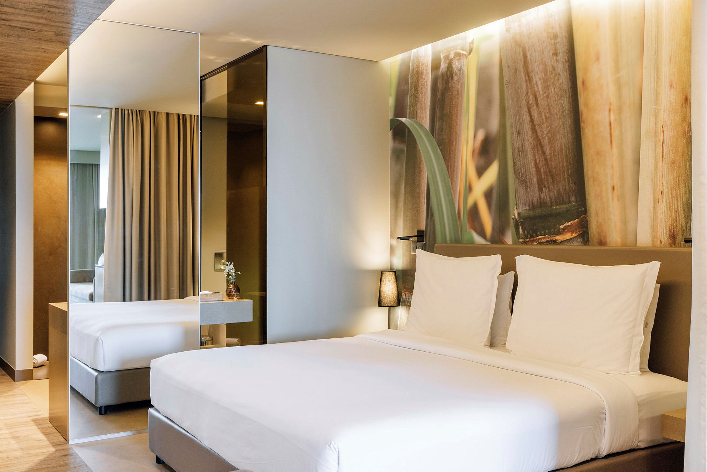 Ett modernt hotellrum med en stor säng med vita sängkläder och en dekorativ vägg med naturmotiv. (AI-genererad text)