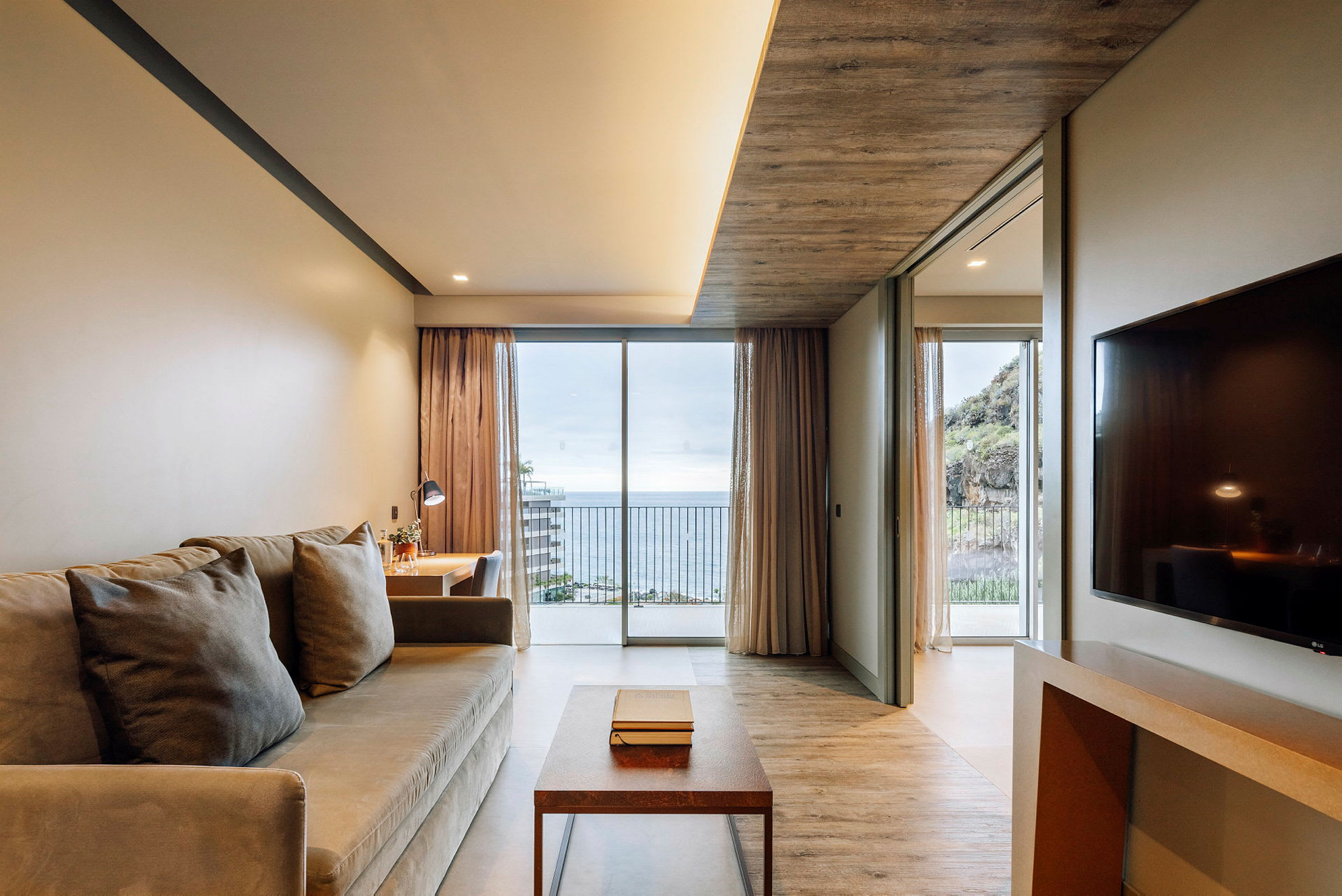 Ett hotellrum med soffa, bord, skrivbord och utsikt över havet genom stora fönster. (AI-genererad text)