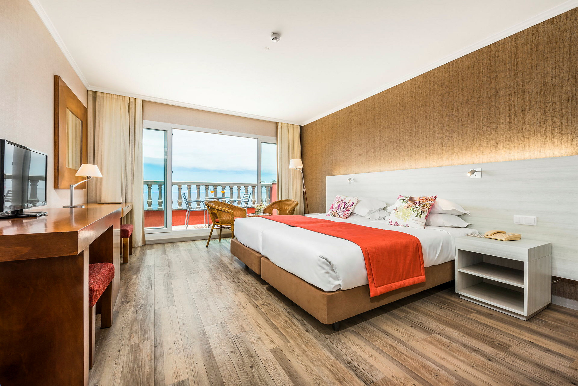 Hotellrum med två sängar, ett bord och utsikt över en balkong och havet. (AI-genererad text)
