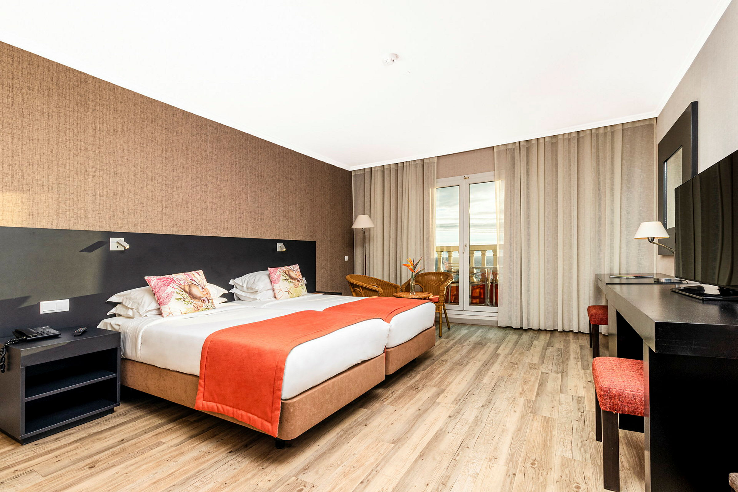 Ett hotellrum med två sängar, skrivbord, TV och sittgrupp. Fönster med utsikt och gardiner syns i bakgrunden. (AI-genererad text)
