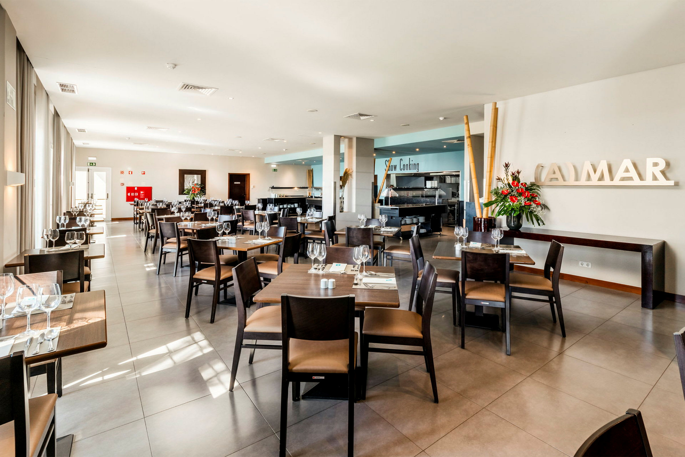 En ljus och modern restaurang med bord och stolar prydligt arrangerade, färska blommor och stora fönster. (AI-genererad text)