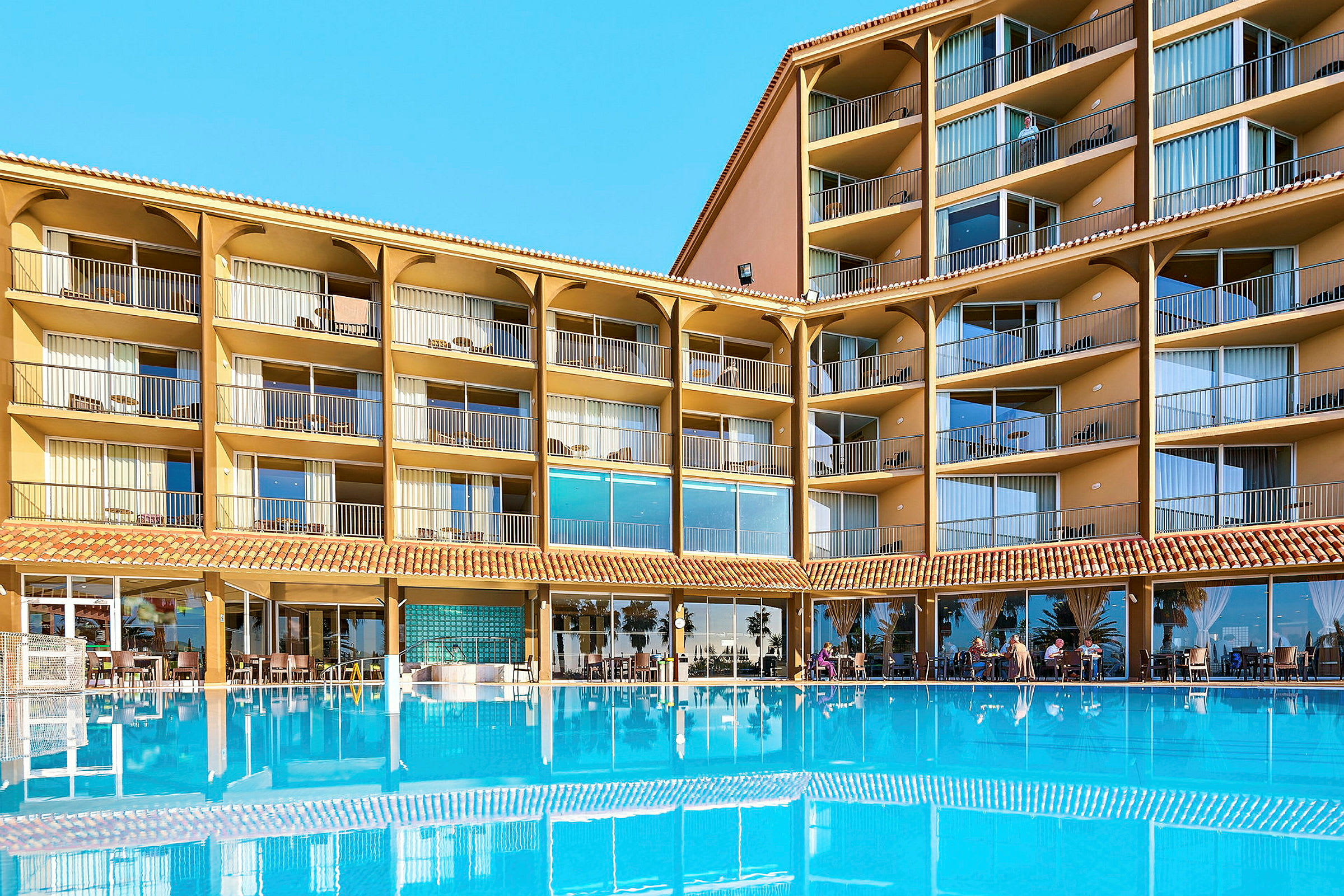 Hotellbyggnad med flera våningar och balkonger, framför en stor blå pool. (AI-genererad text)