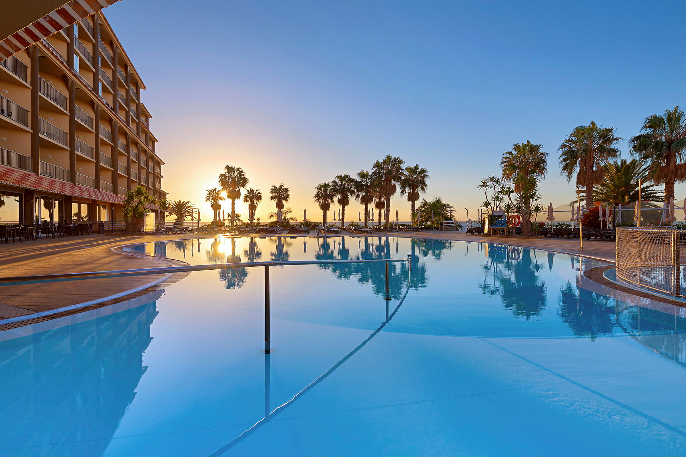 Poolområde vid hotell med palmträd och solnedgång. (AI-genererad text)
