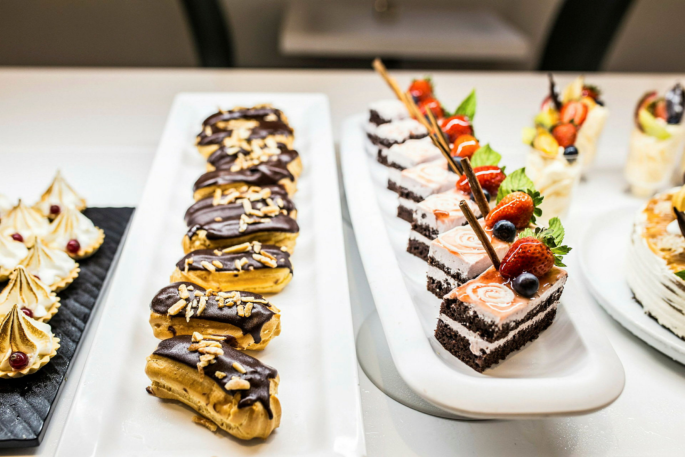 Ett bord med olika desserter, inklusive chokladtäckta eclairs och tårtbitar med fruktdekor. (AI-genererad text)