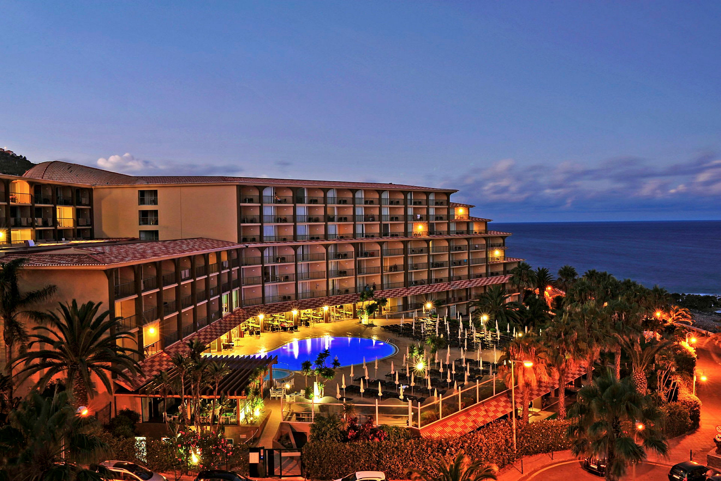 Hotellbyggnad vid havet med belysning och pool. (AI-genererad text)