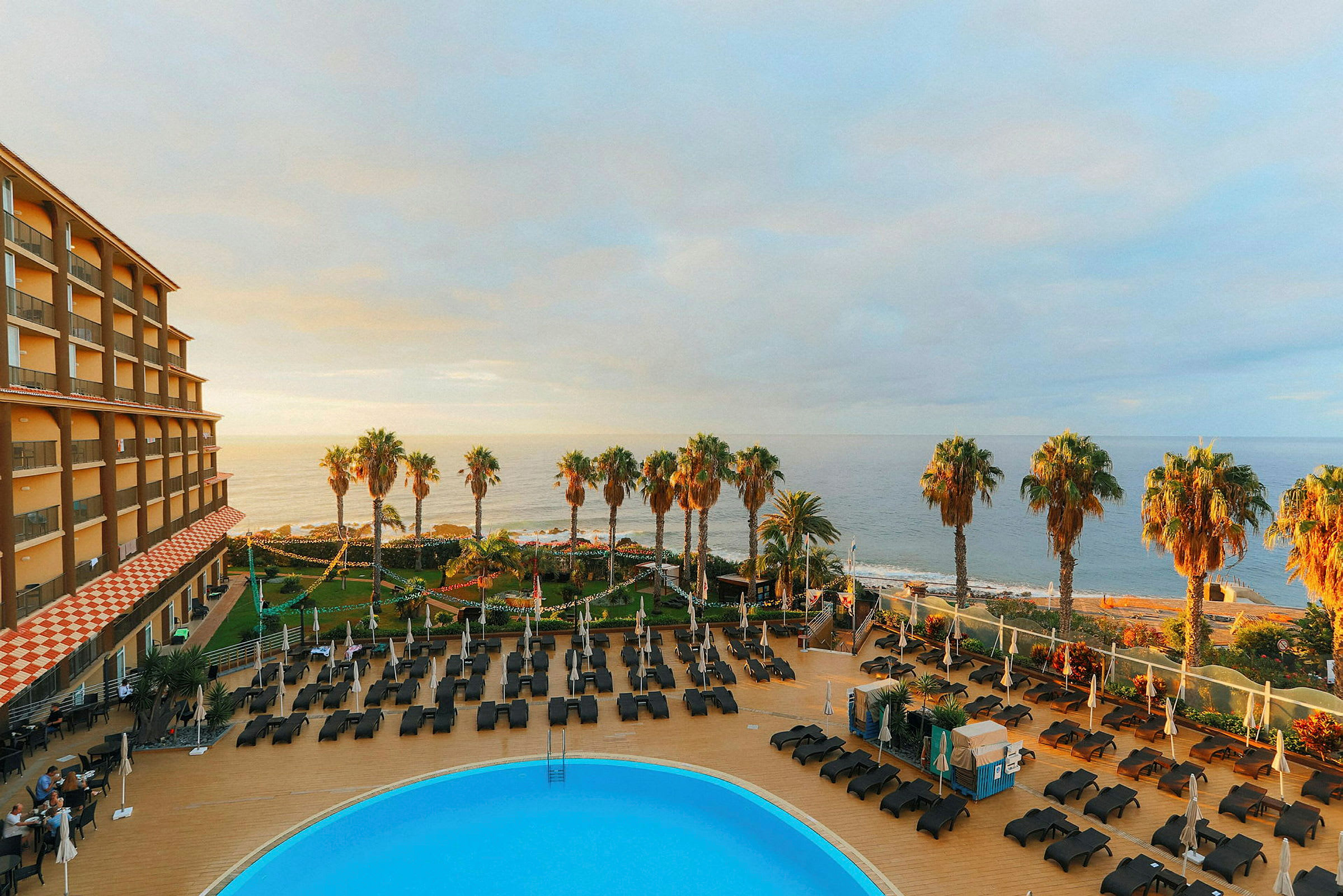 Bild av hotellområde med pool, solstolar och palmer nära havet. (AI-genererad text)