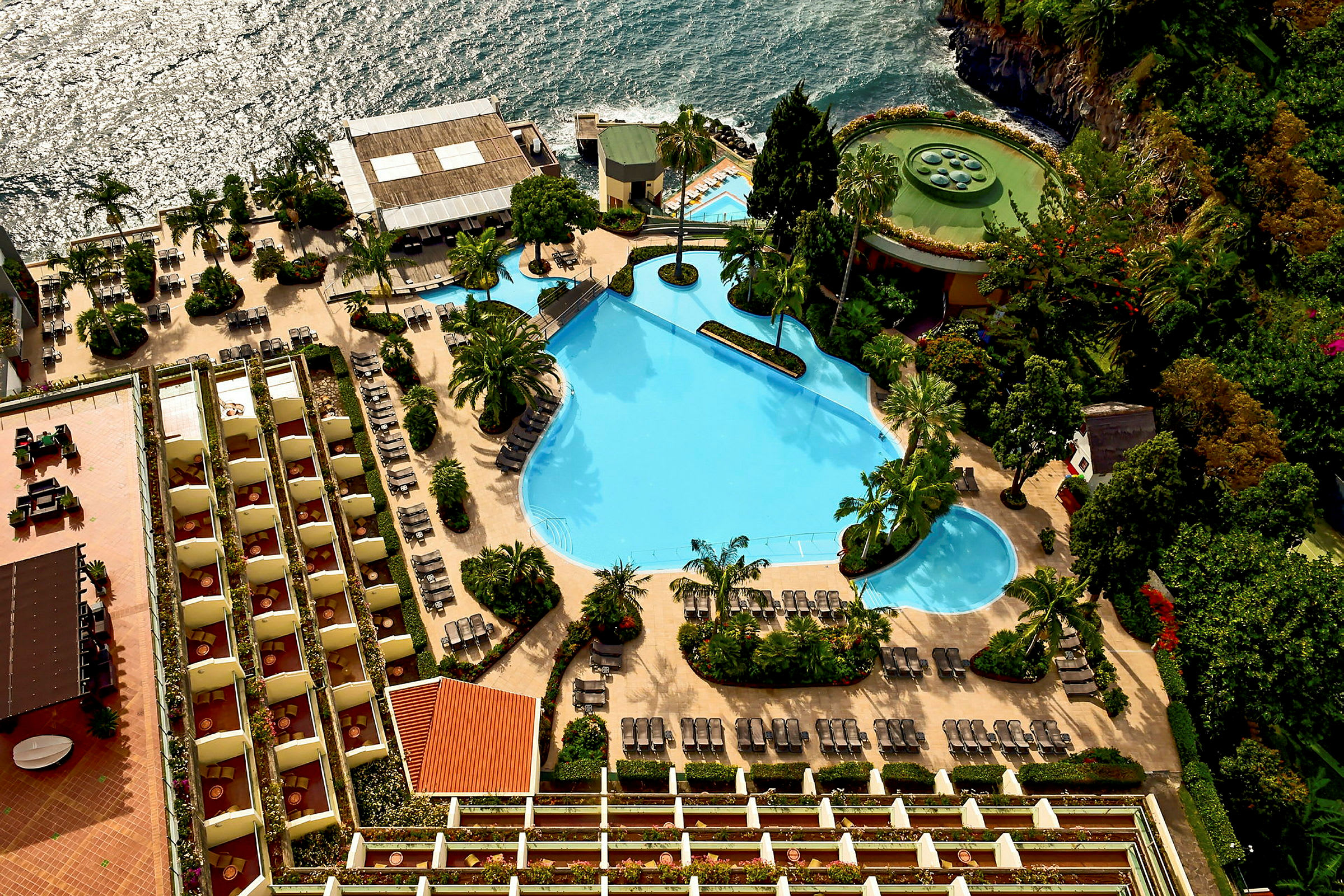 Bild av en hotellpool med solsängar, omgiven av grönska och terrasser. Bakgrunden visar ett hav. (AI-genererad text)