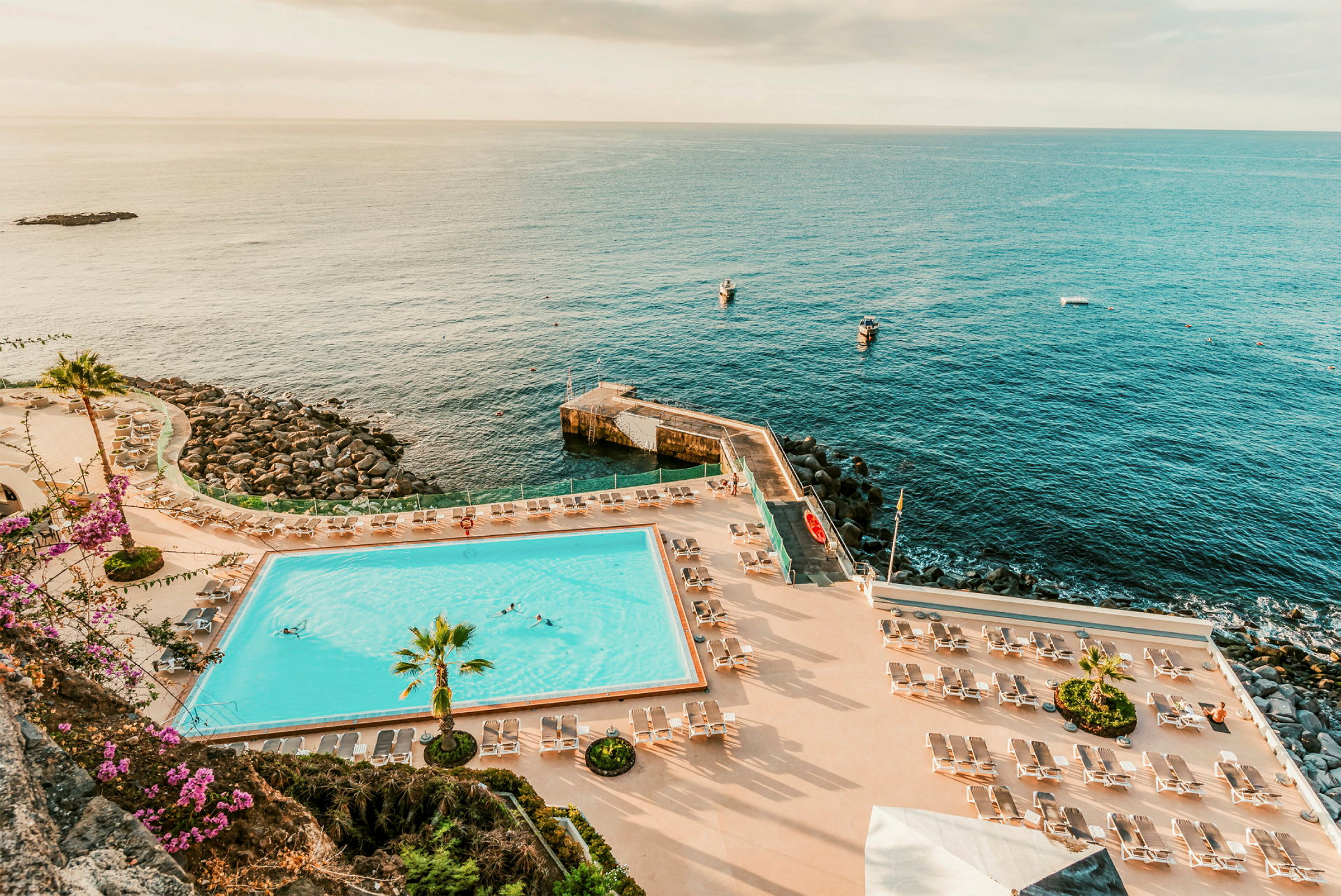 En pool med solstolar runtom och utsikt mot havet. (AI-genererad text)