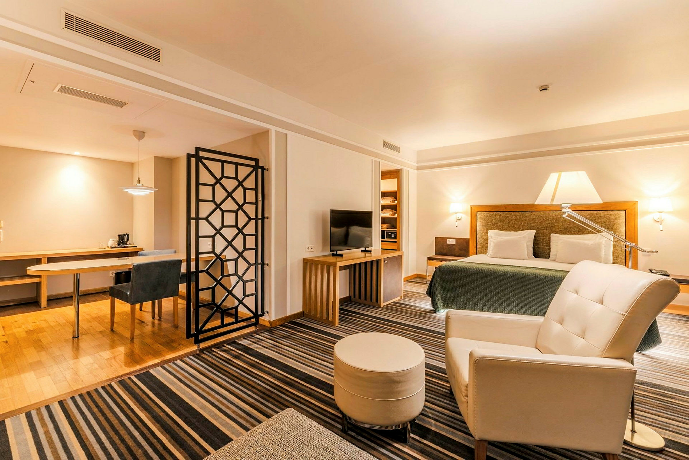 Ett hotellrum med en dubbelsäng, TV, fåtölj och ett arbetsområde. Rummet har en modern inredning med ljusa färger. (AI-genererad text)