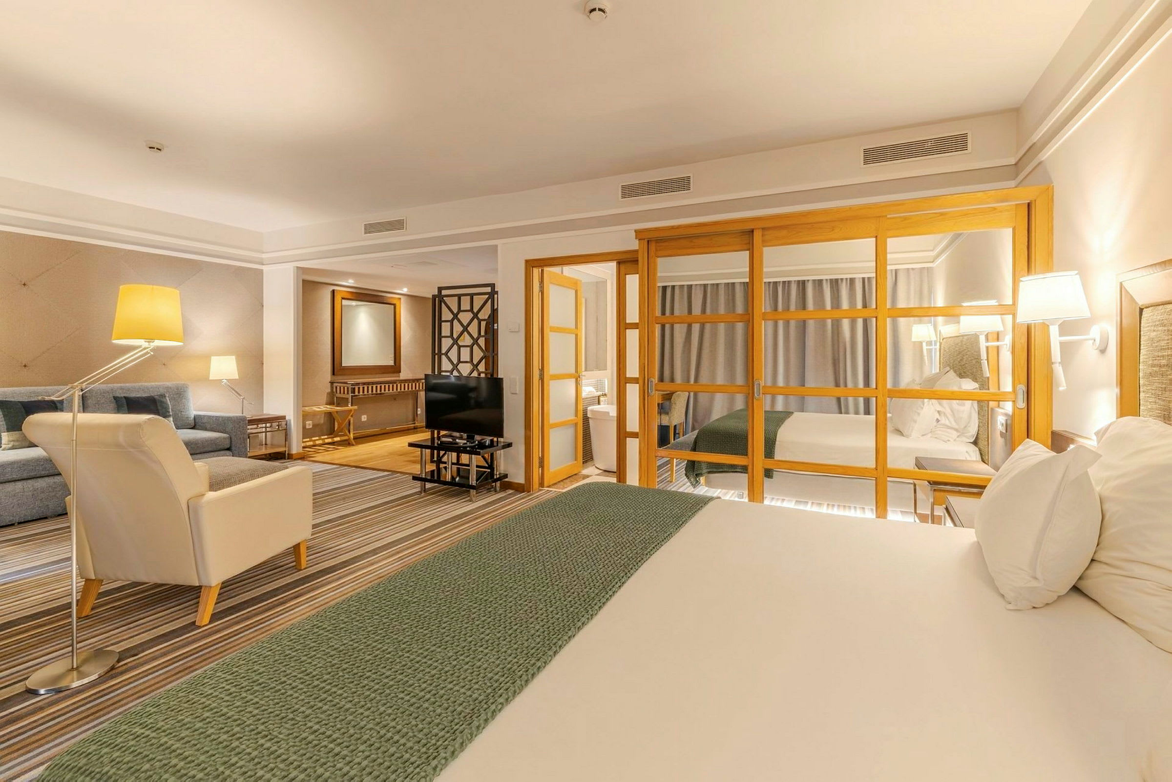 Ett hotellrum med en sittgrupp, en säng och glasdörrar som separerar rummen. (AI-genererad text)