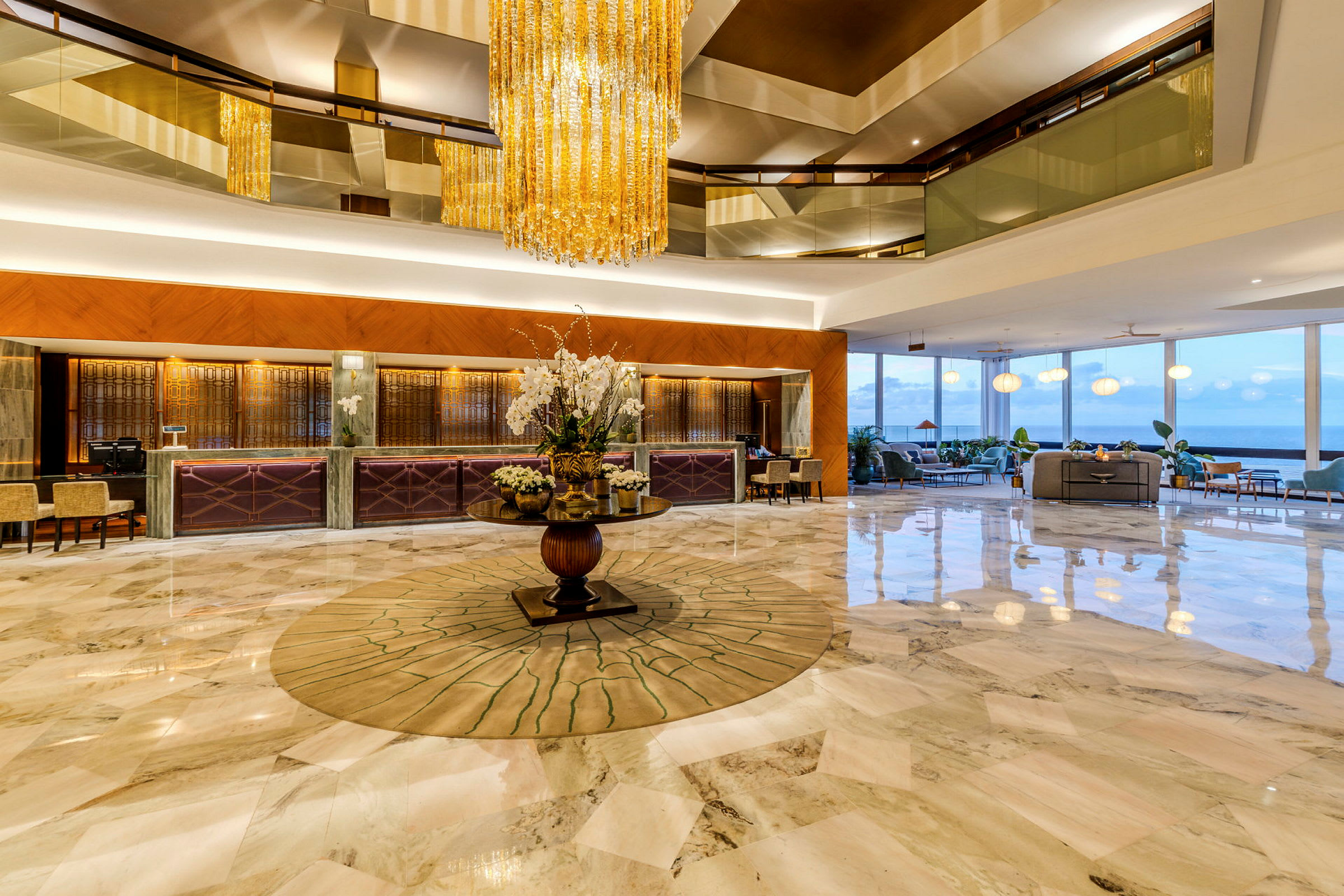 Ett elegant hotellobby med ett stort golv i marmor, en central dekoration med blommor och en kristallkrona hängande från taket. (AI-genererad text)