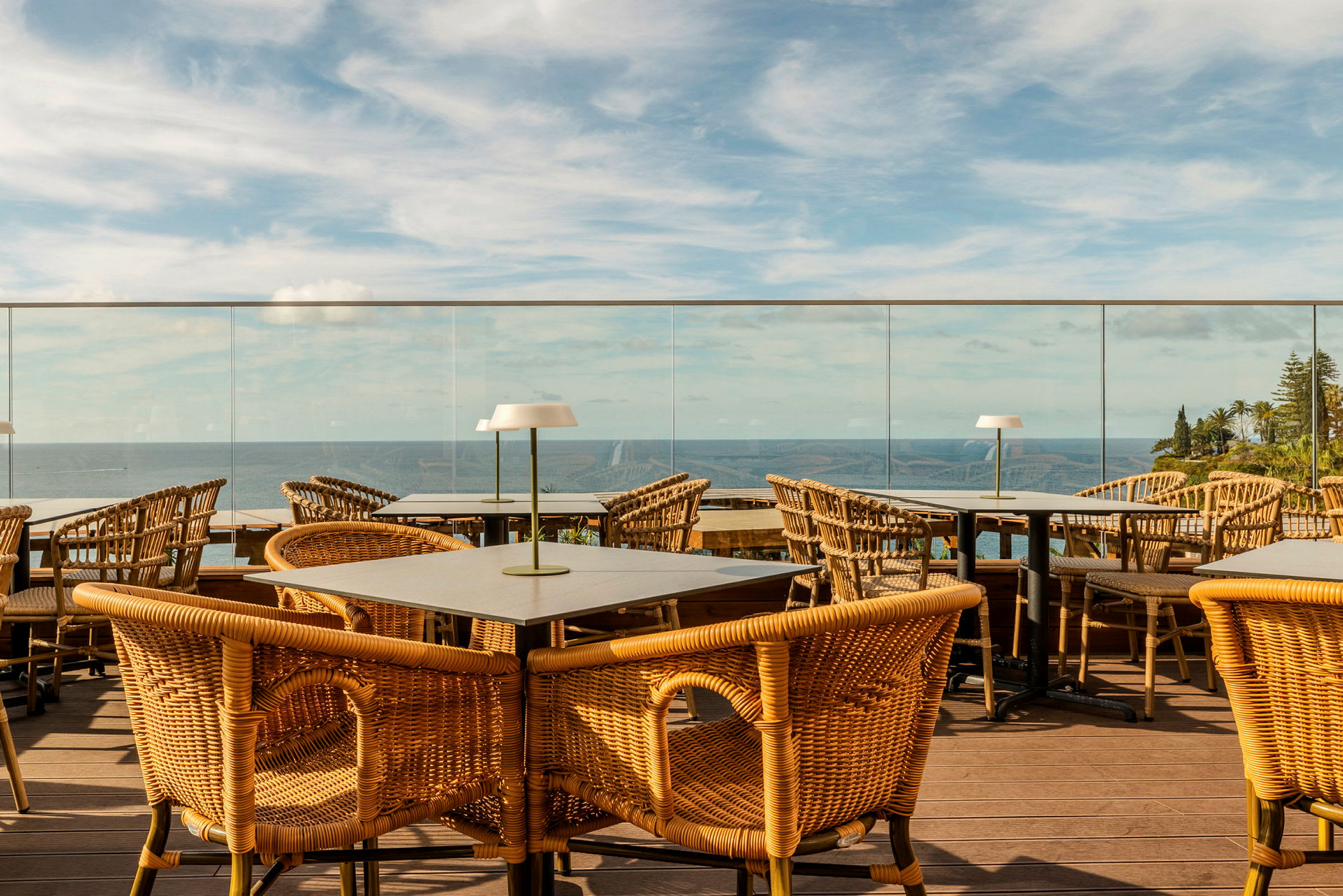 En terrass med bord och rottingstolar med utsikt över havet och omgivande landskap. (AI-genererad text)